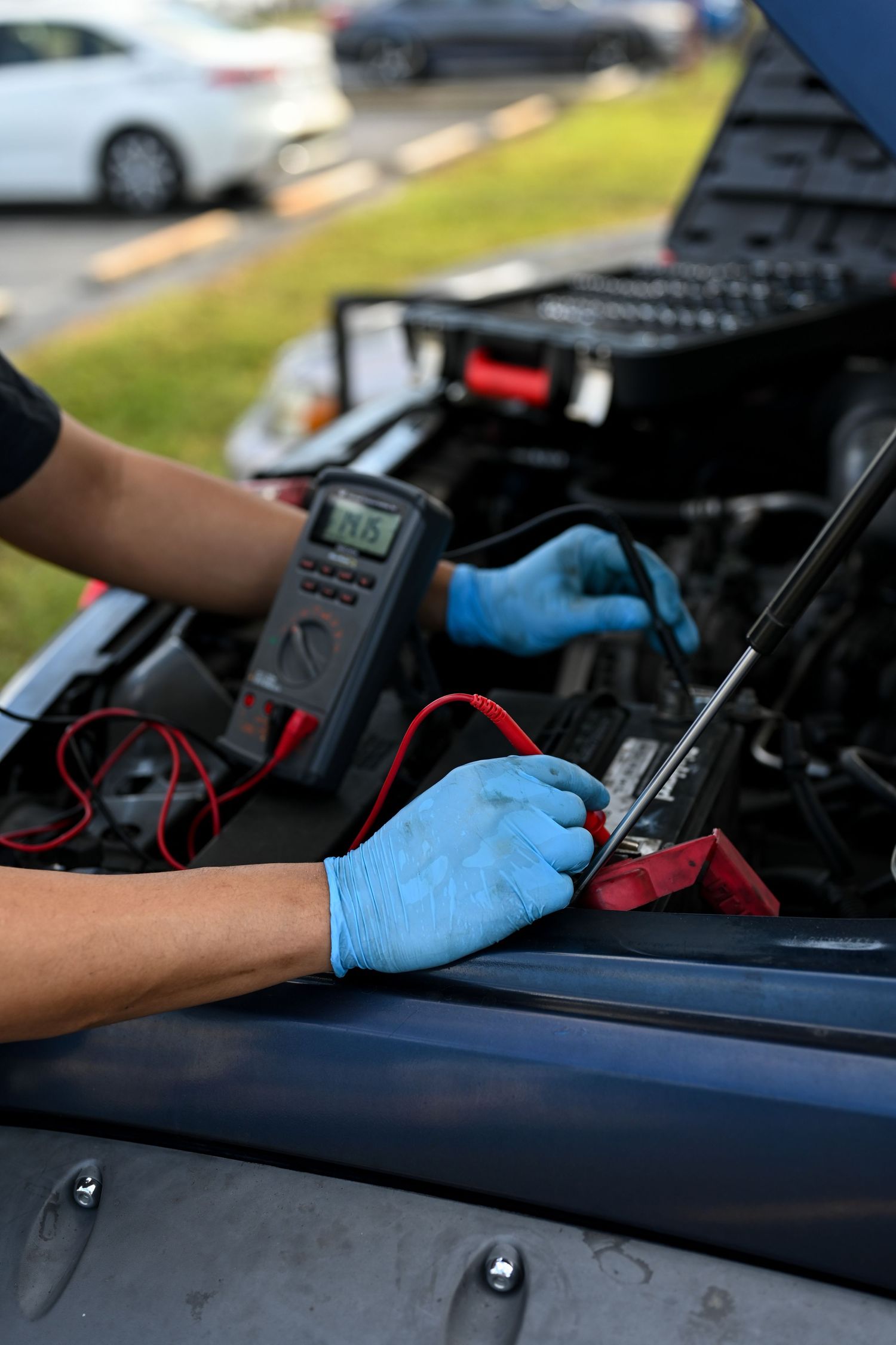 Close-up of hands in blue gloves performing electrical testing on car engine.