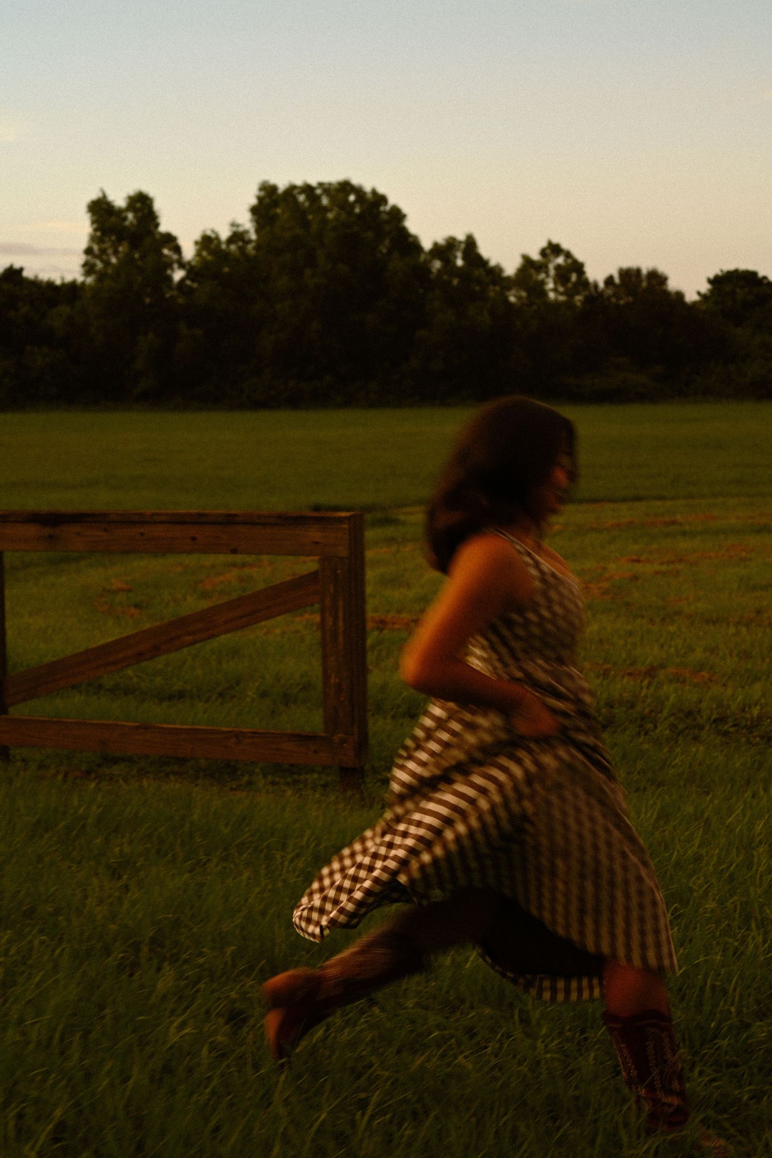 Figure in gingham dress leaps gracefully across a grassy field at sunset.