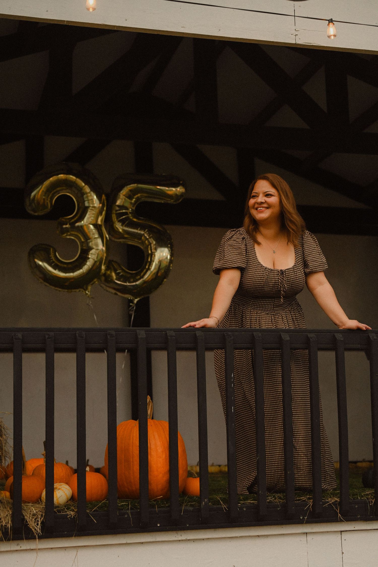 Dark wooden balcony decorated with gold number balloons and pumpkins for autumn celebration.
