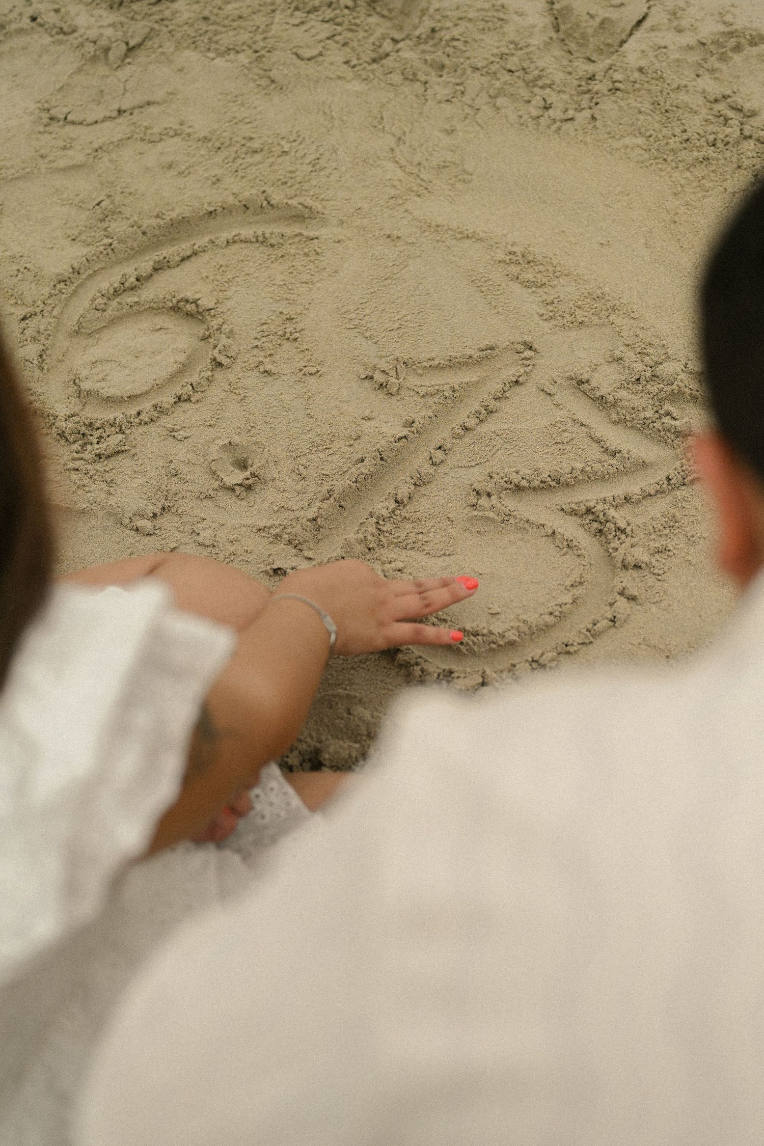 Writing messages in the sand at the beach with hands visible in the frame.