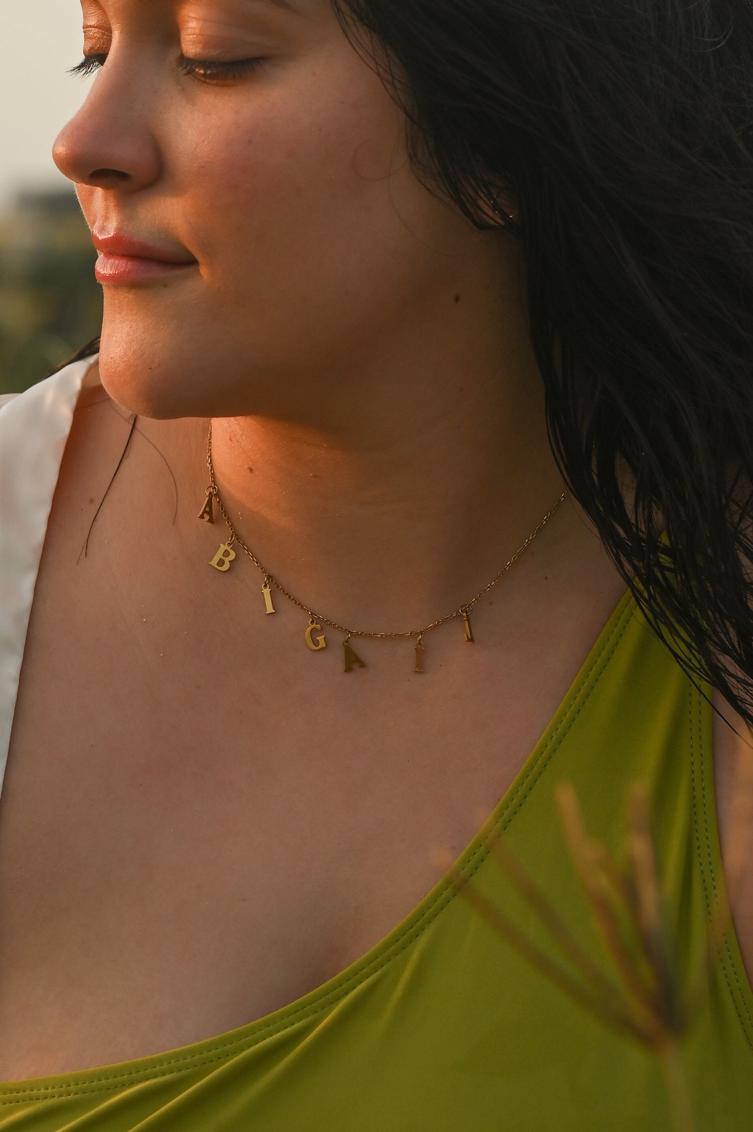 Close-up profile view wearing a chartreuse top and delicate gold necklace in natural lighting.
