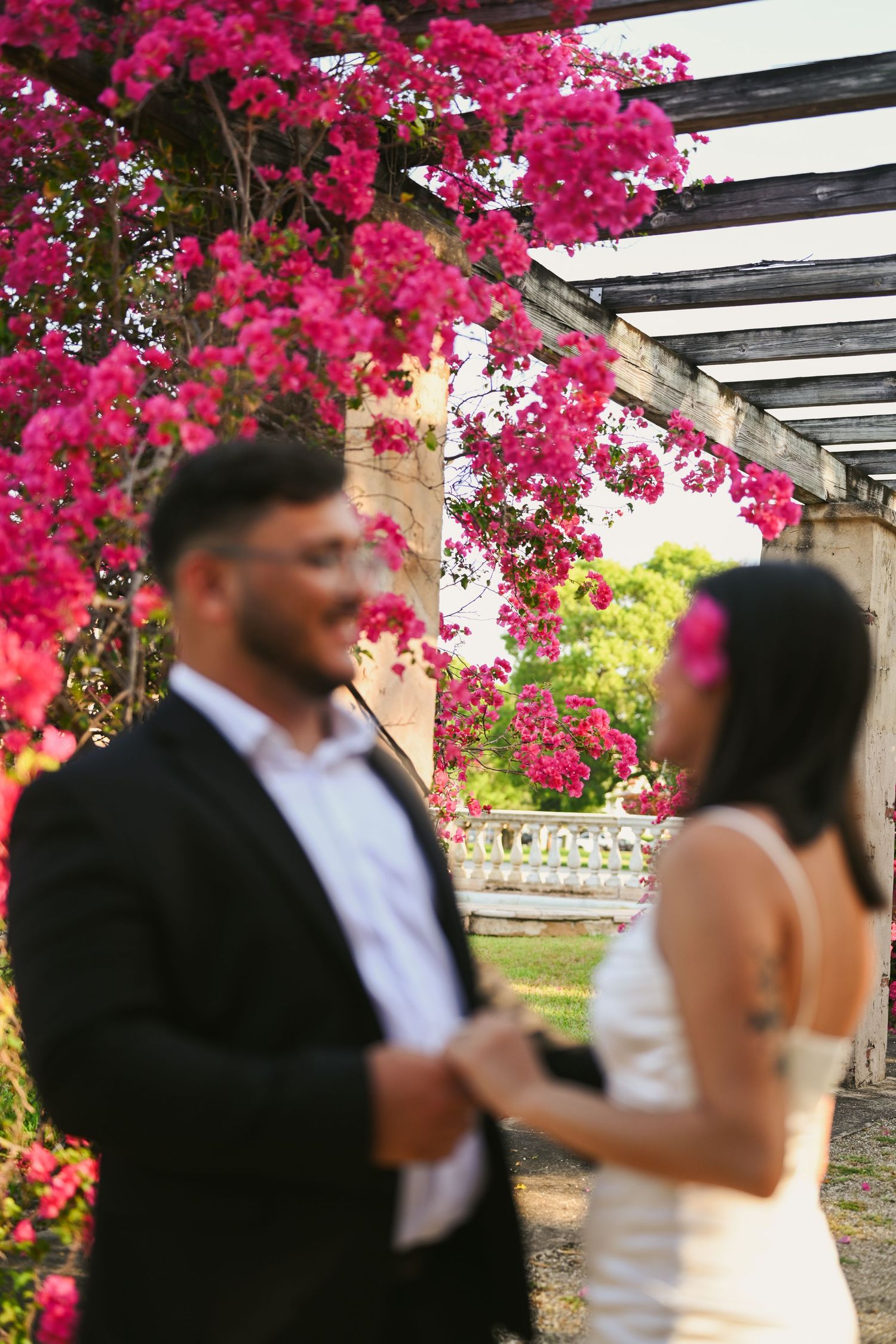 Artistic blurred shot of couple beneath pergola with vibrant pink flowers.