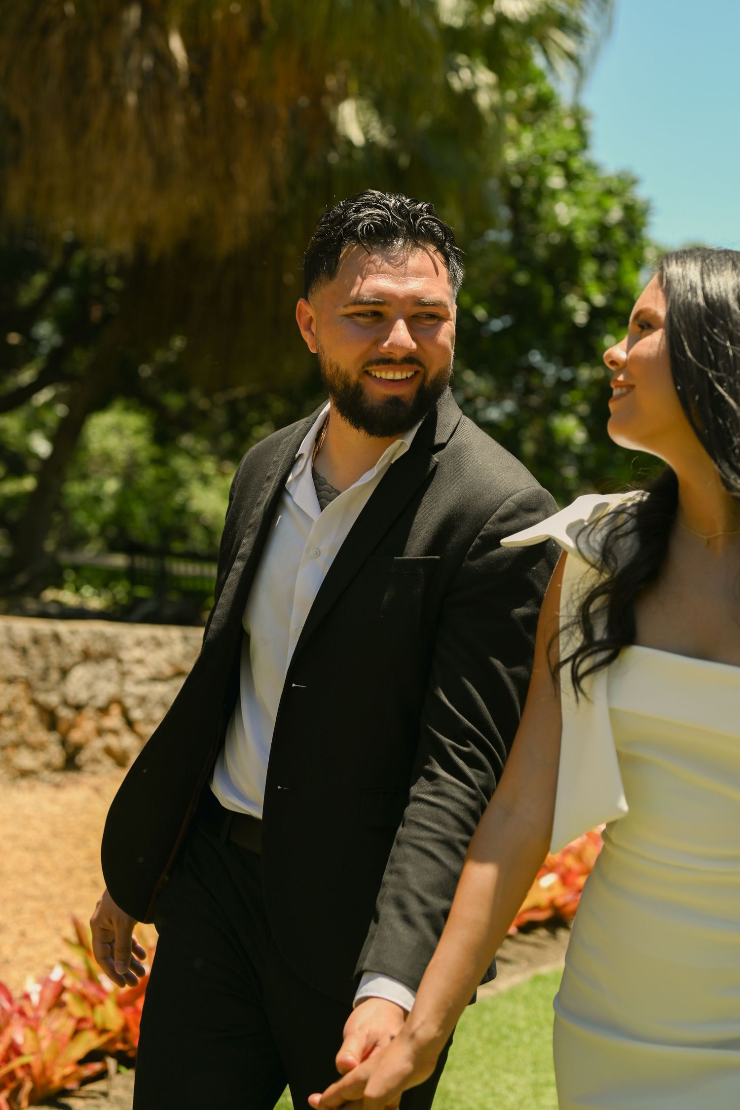 A couple shares joyful laughter while embracing in a sunny garden setting.