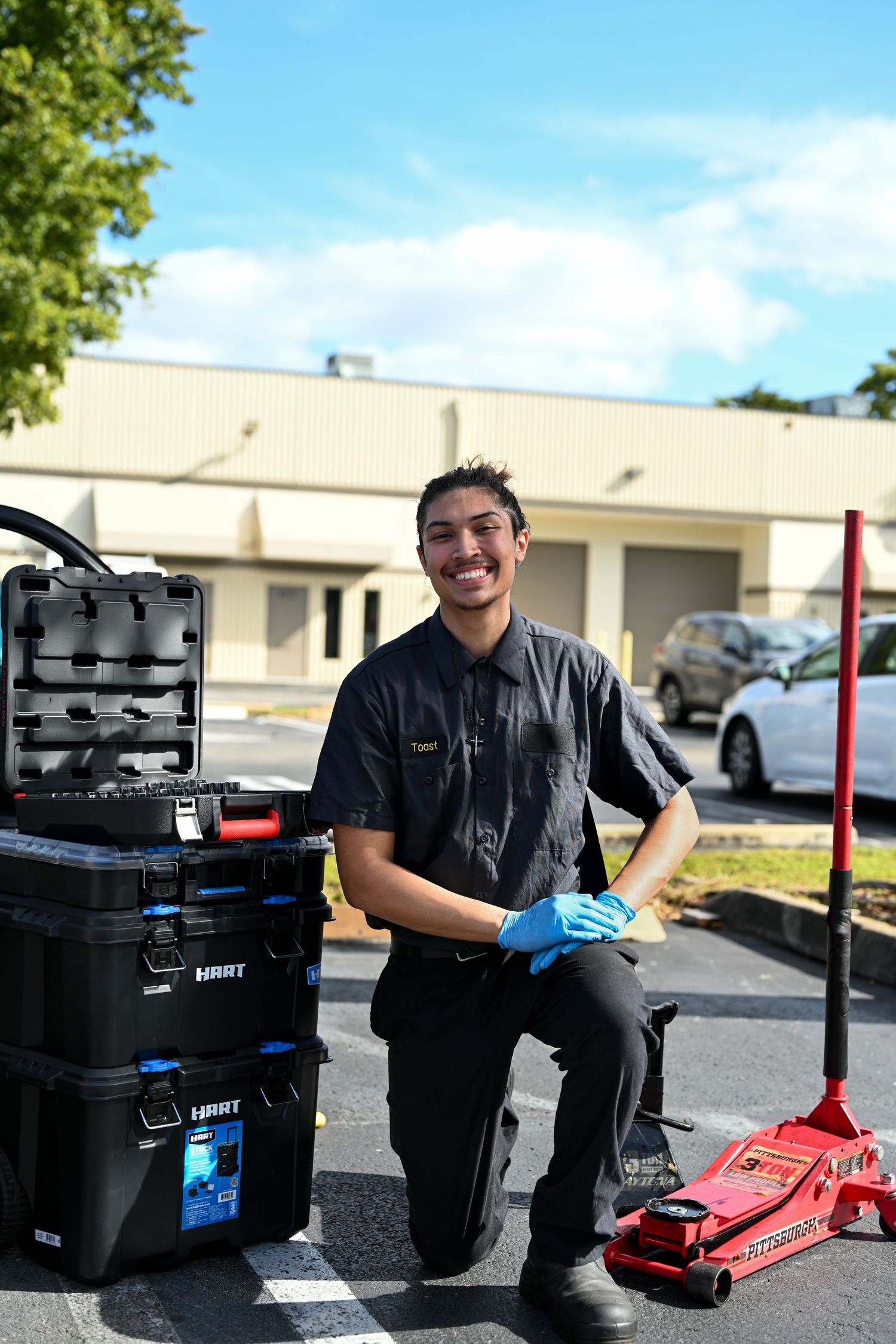 Mechanic kneeling next to automotive tools and equipment in a service area.