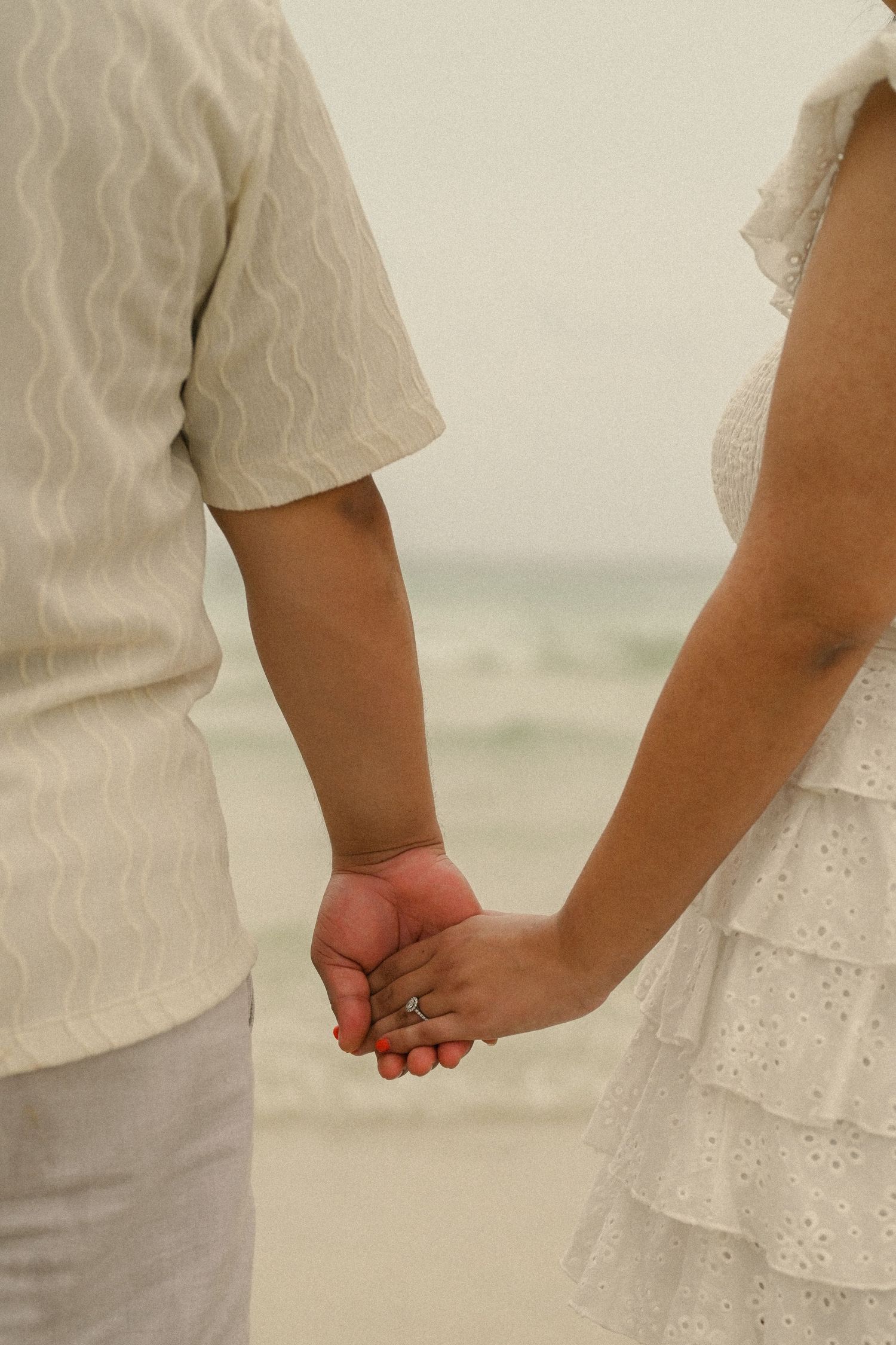 Close-up shots of a couple holding hands while wearing coordinated white outfits.