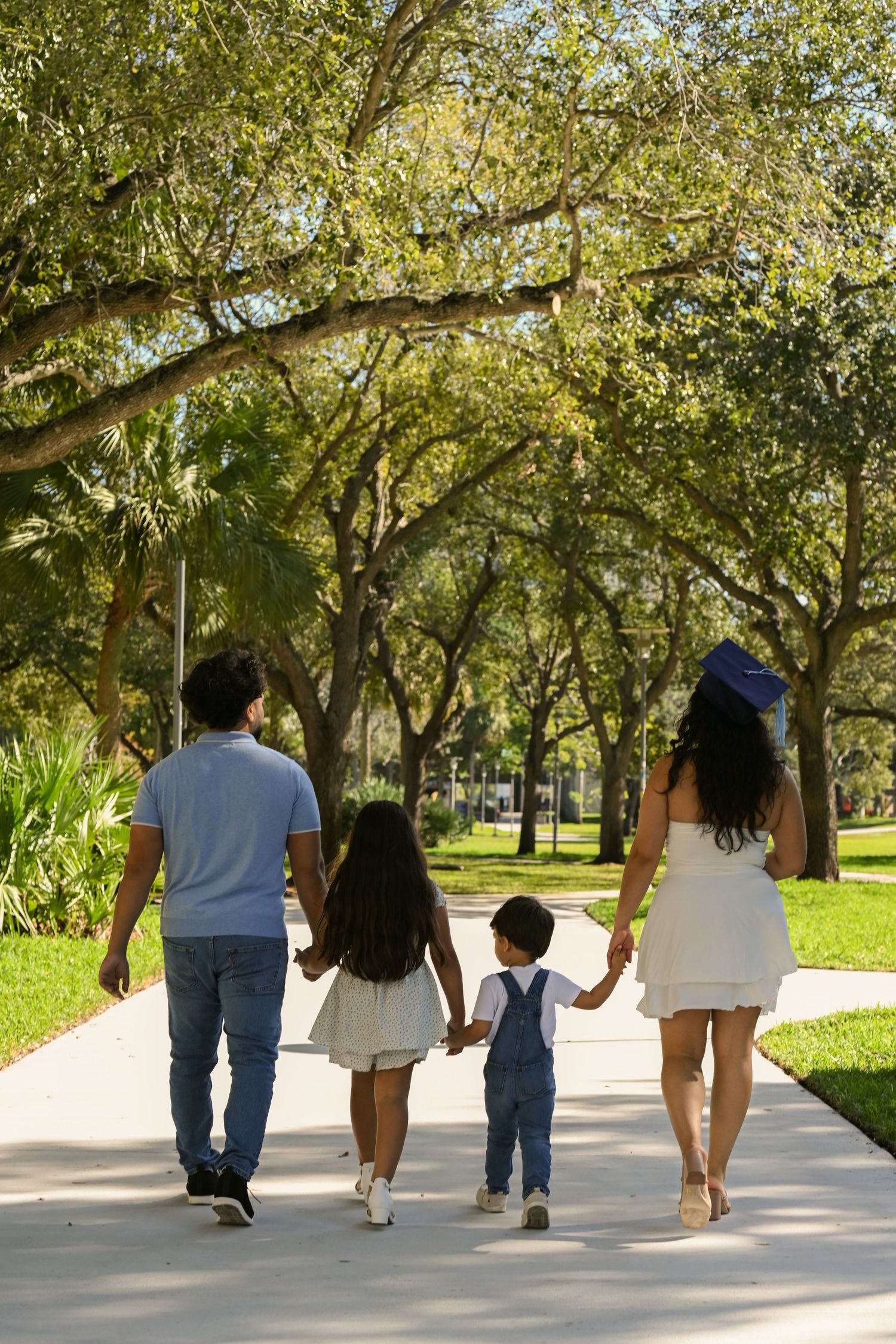 A family walking together on a tree-lined path on a sunny day.