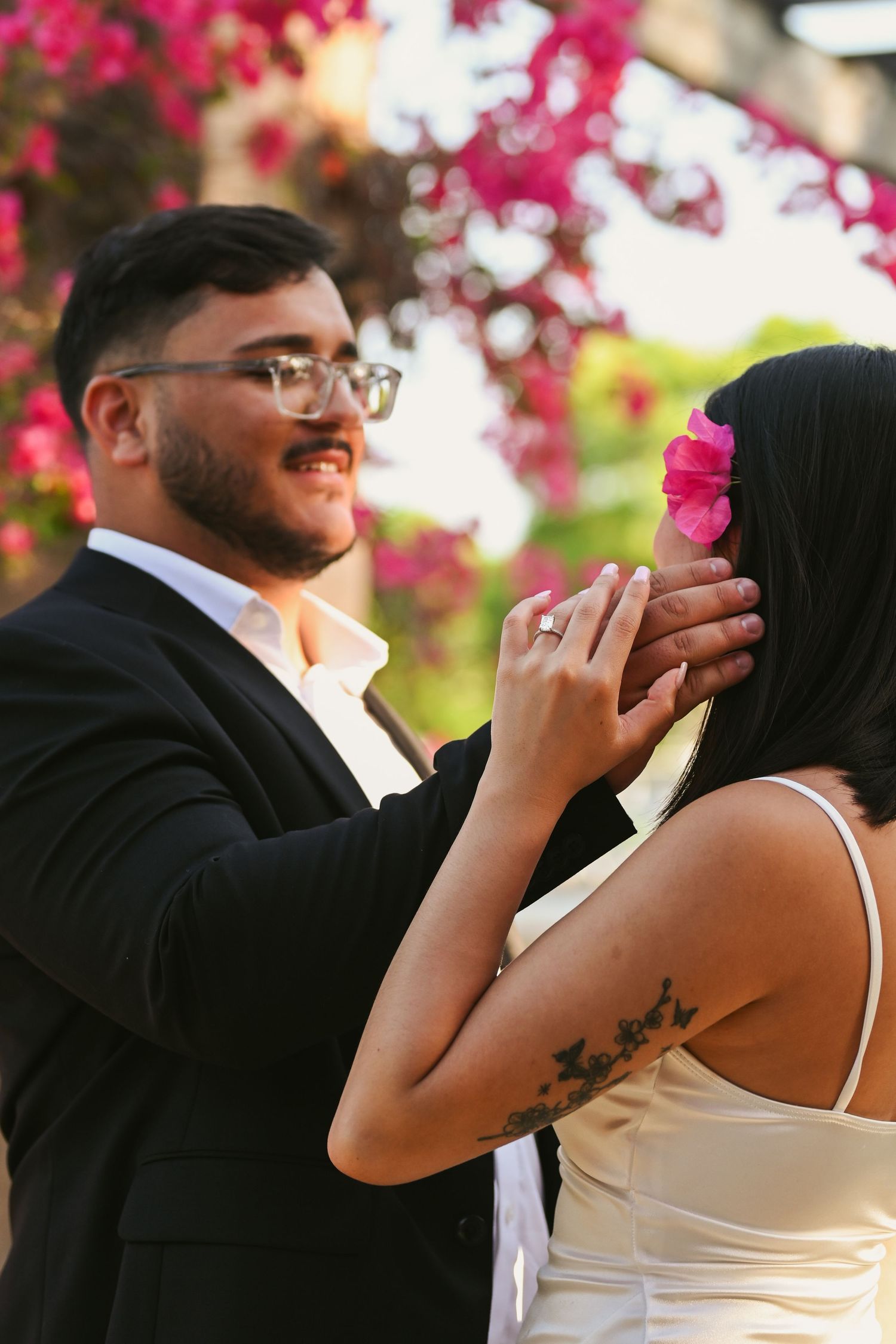 Candid moment captured between couple under pink bougainvillea blooms.