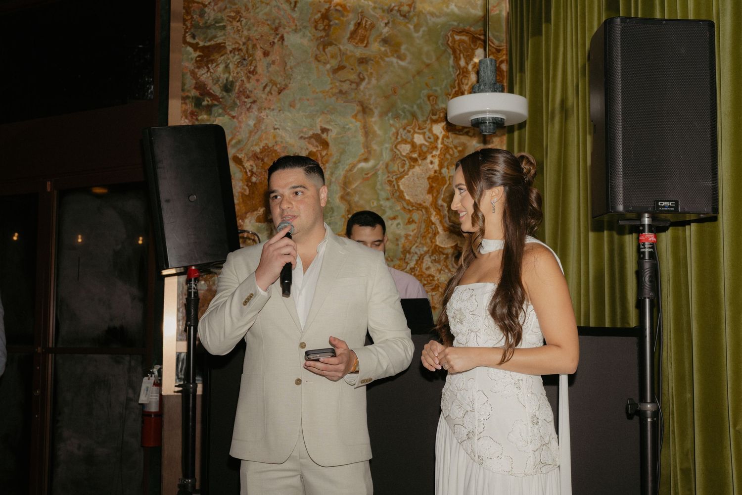 Bride and groom speaking into microphone at wedding reception in elegant venue.