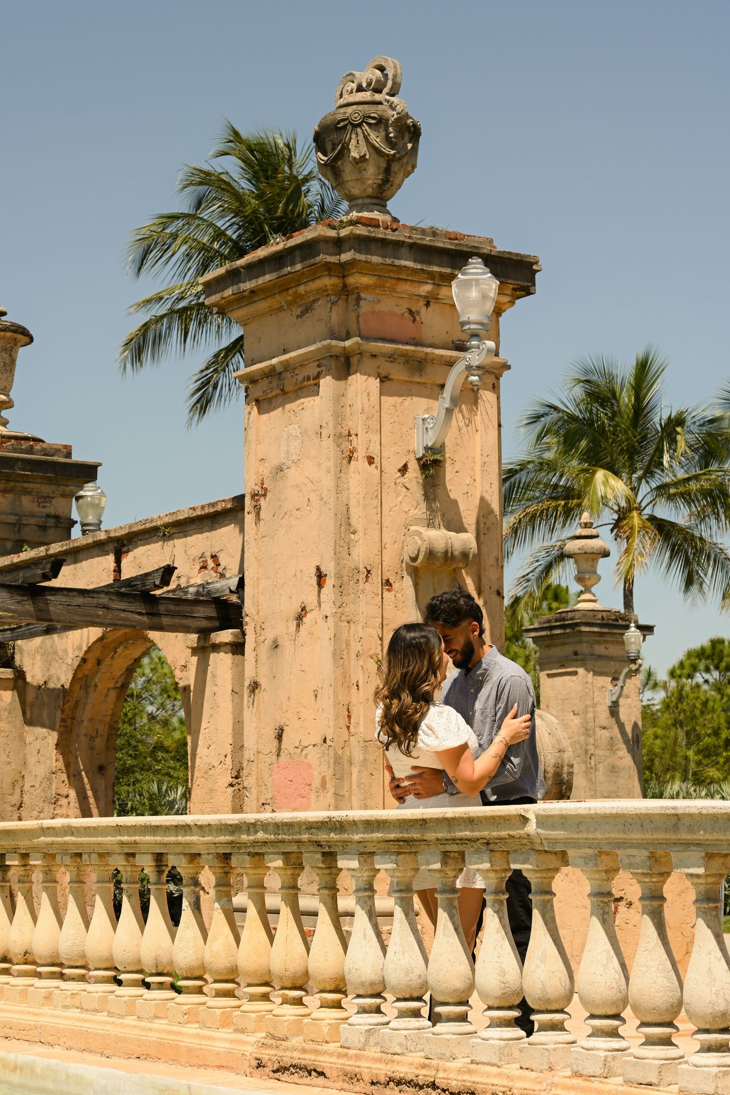 A romantic moment captured against historic architecture with palm trees and blue sky.