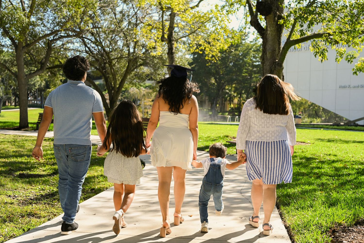 People walking together on a sunny campus pathway surrounded by green grass and trees.