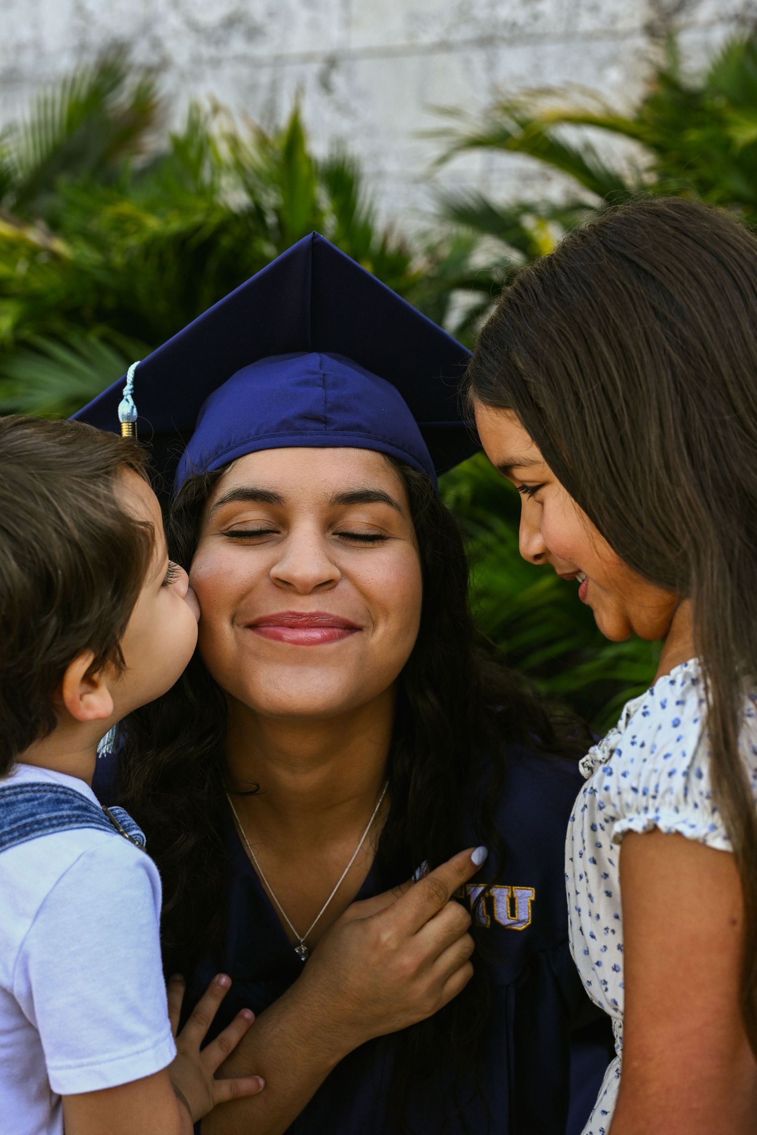 Heartwarming graduation moment shared between graduate and children against stone wall.