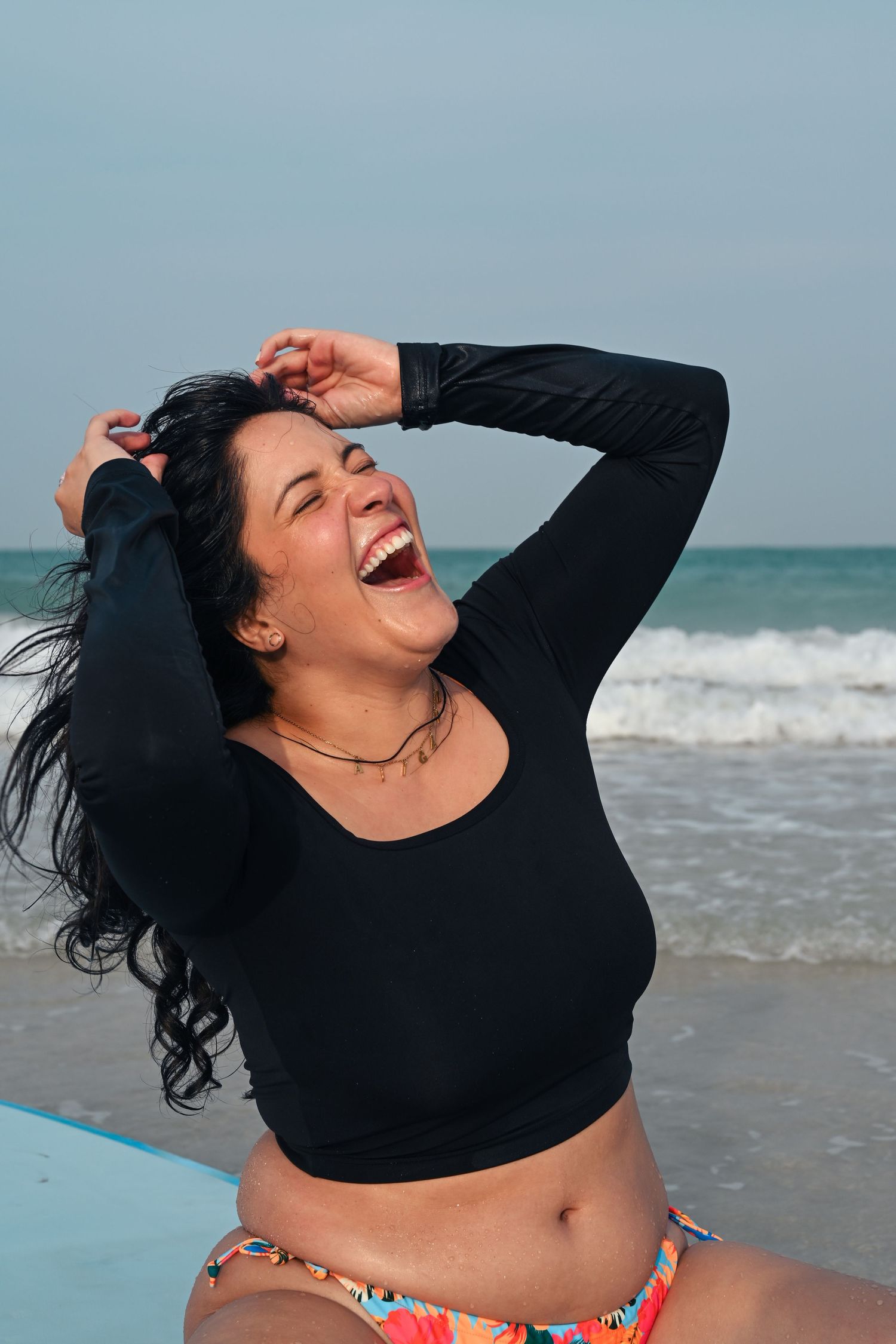 Person in black long sleeve top laughing joyfully at the beach with waves in background.