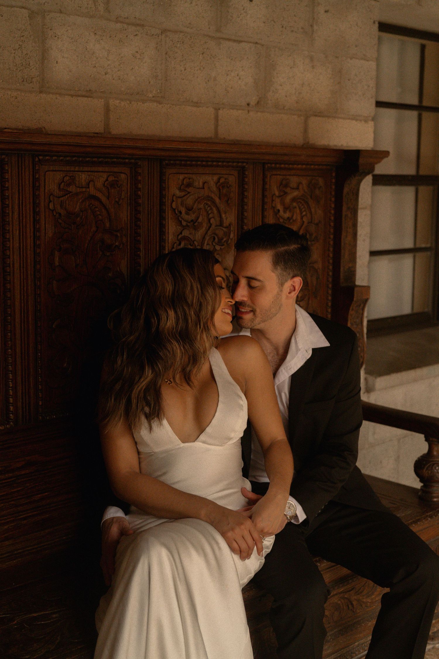 Romantic couple nearly kissing on an ornate carved wooden bench during an intimate engagement photo session.