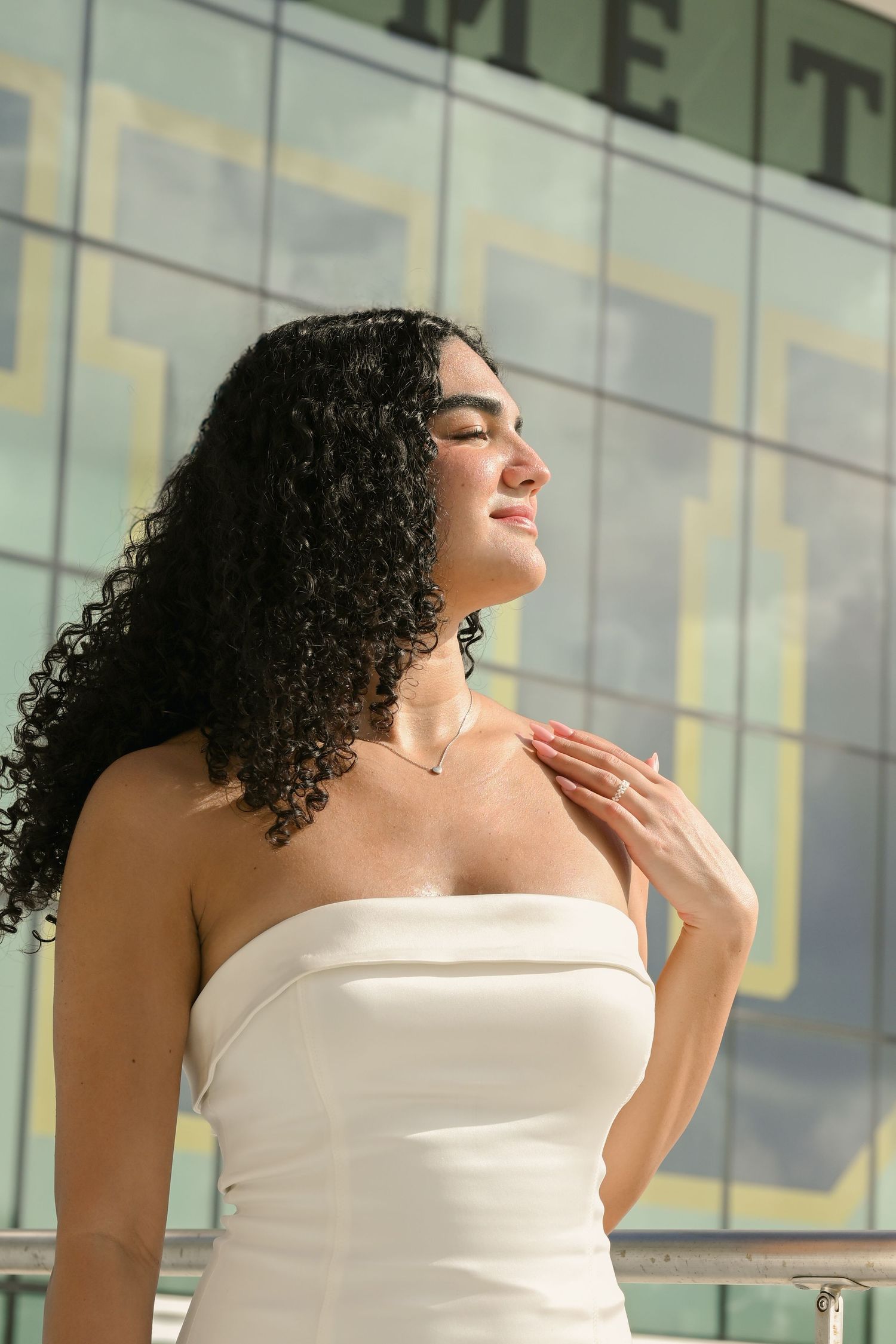 Person in white dress poses elegantly against modern glass building.