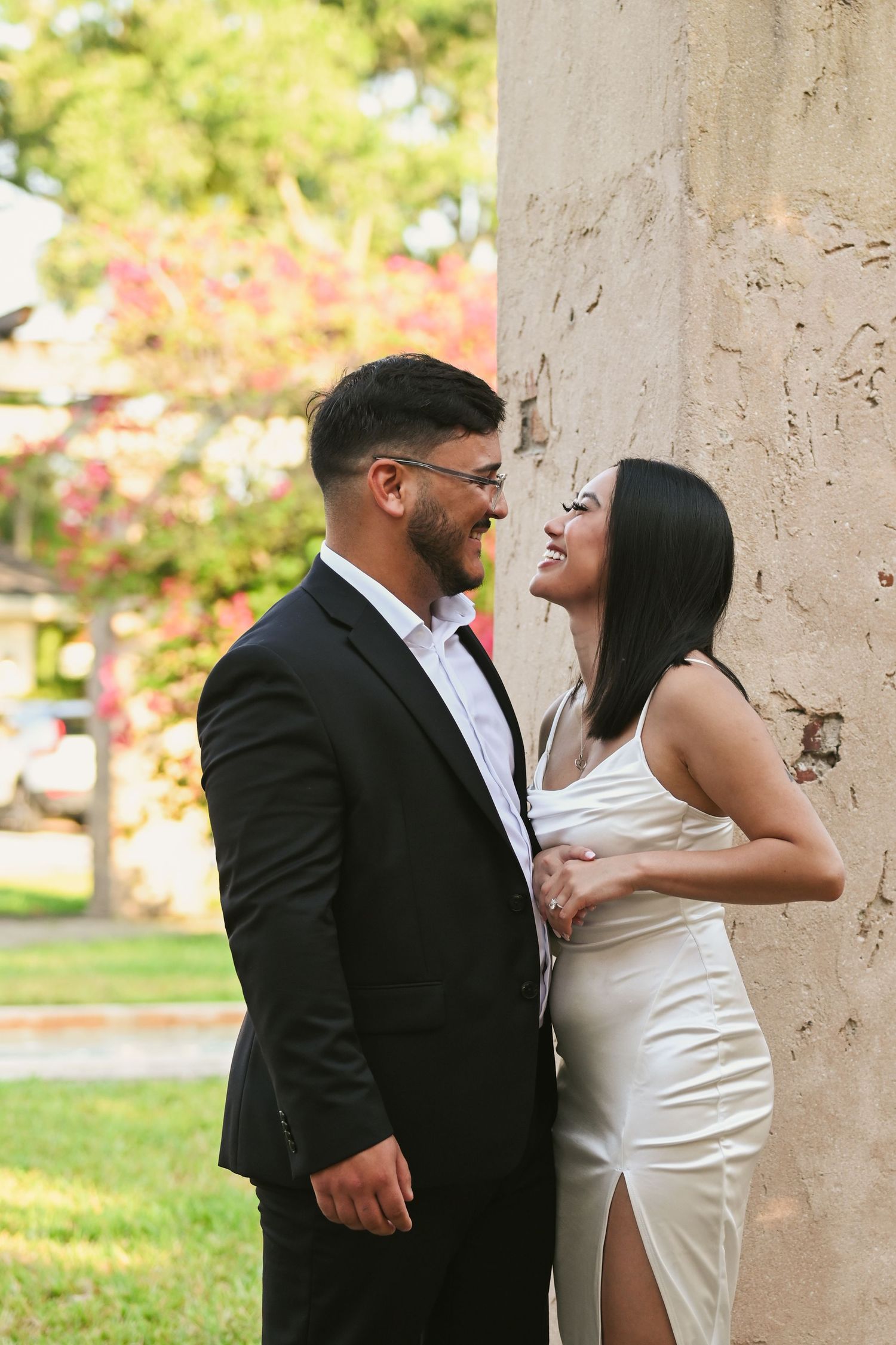 A joyful moment captured between stone columns with bright pink flowers in the background.