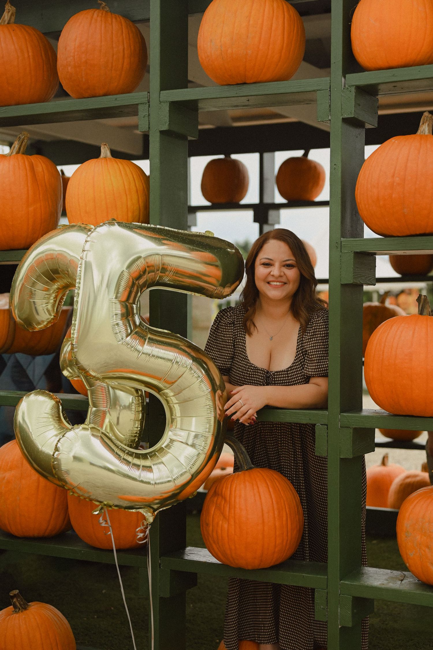 Festive autumn display with orange pumpkins on green shelving and gold number balloons for celebration.