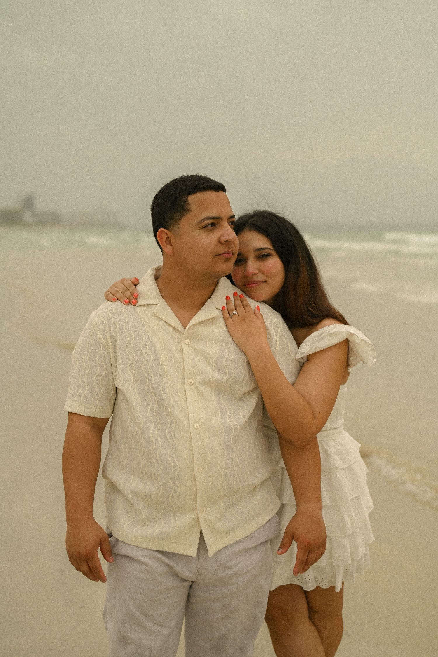 A couple shares a sweet moment together during their beach photoshoot in matching white outfits.