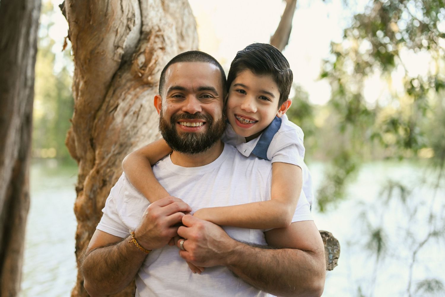 Father and son sharing playful moments outdoors near a lake.