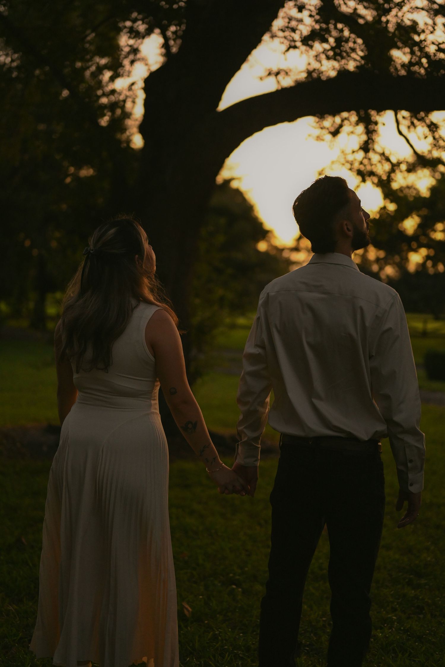 Couple walking hand in hand through park at golden hour.