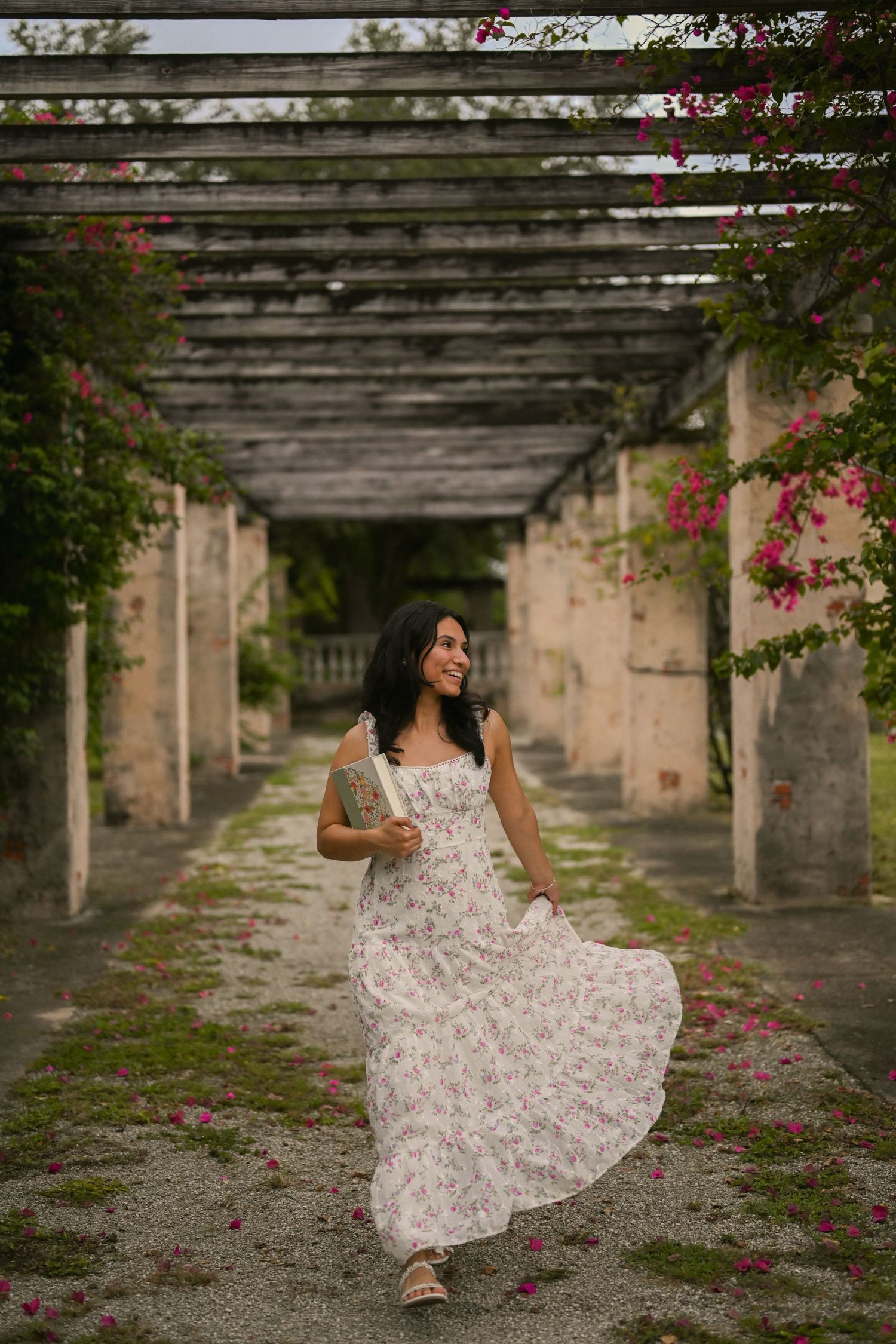 A floral dress twirls beneath a stone colonnade decorated with pink flowering vines.