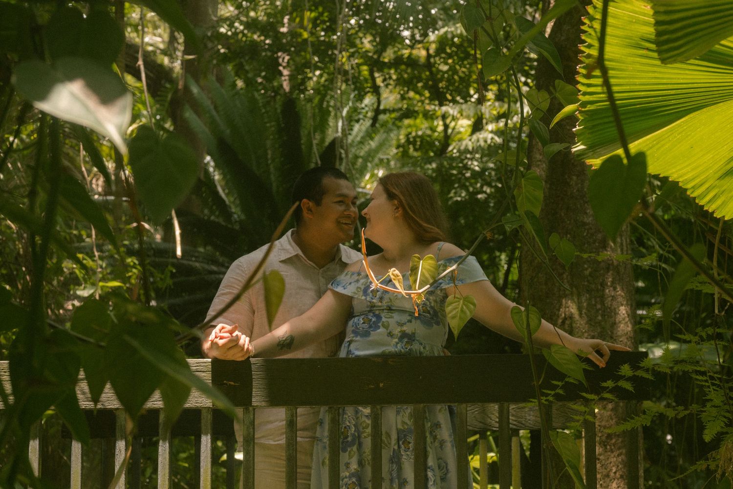 Romantic couple sharing a tender moment on a wooden bridge surrounded by lush tropical greenery.