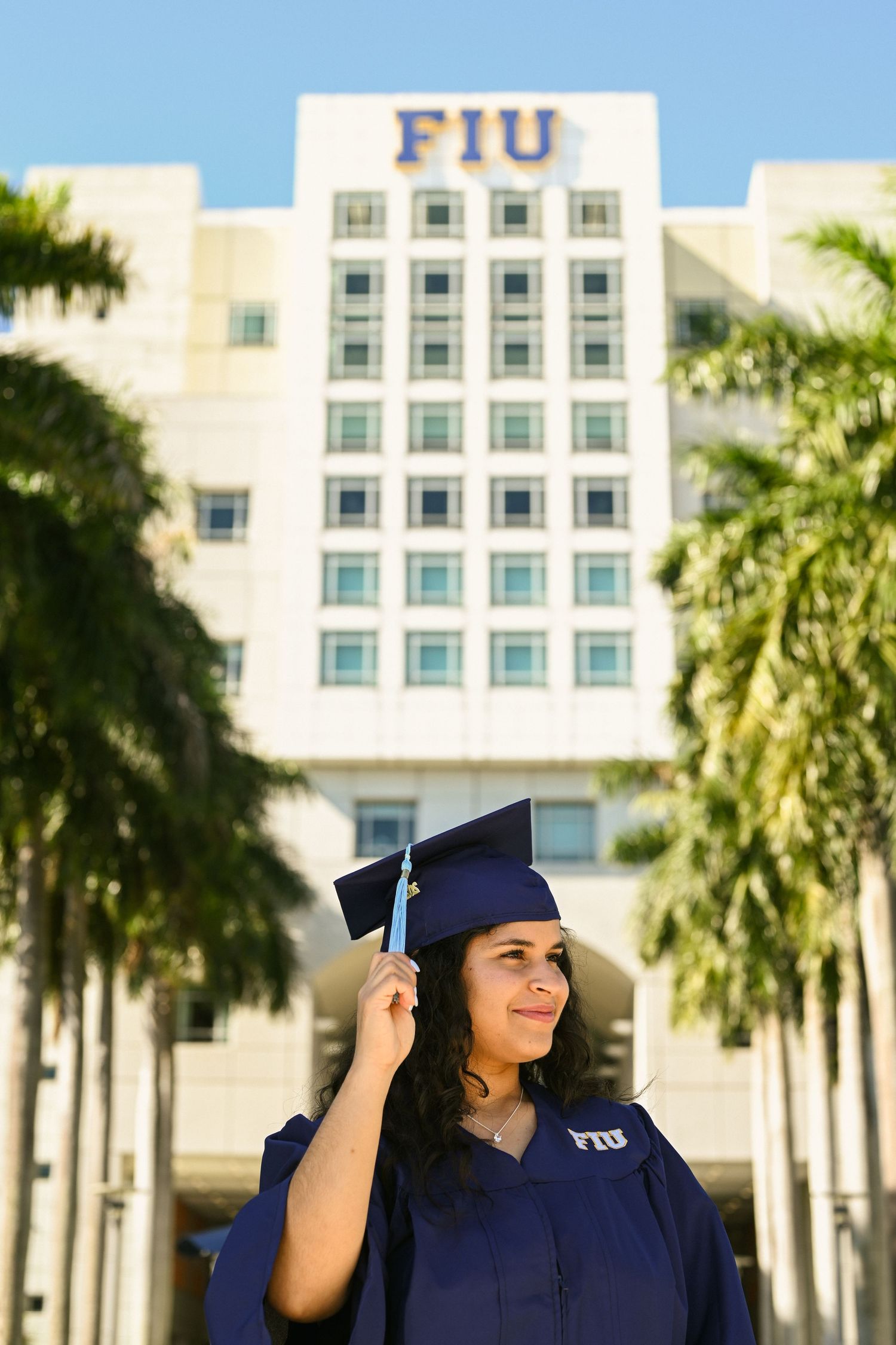 A graduation photoshoot in front of an FIU building with palm trees.