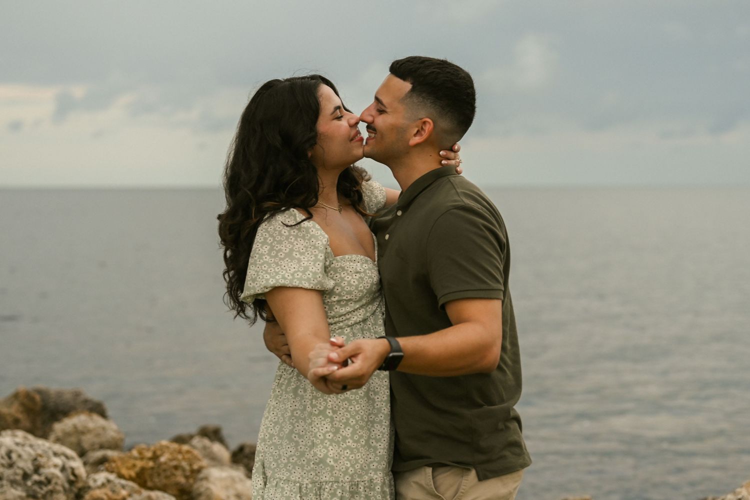 A romantic couple shares tender kisses against an ocean backdrop.