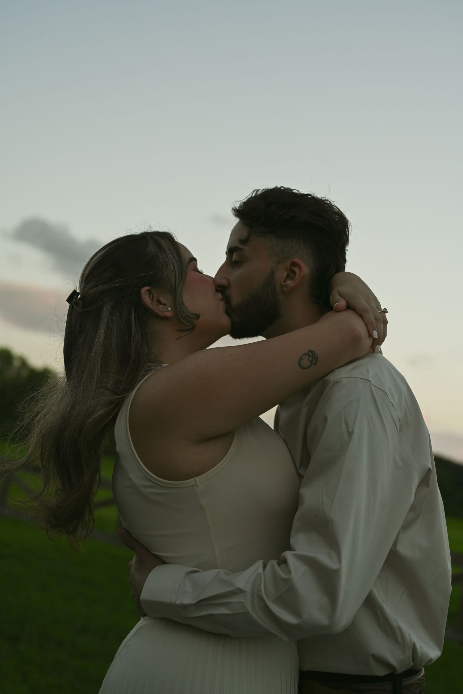 A tender embrace and kiss shared between a couple in a park during golden hour.