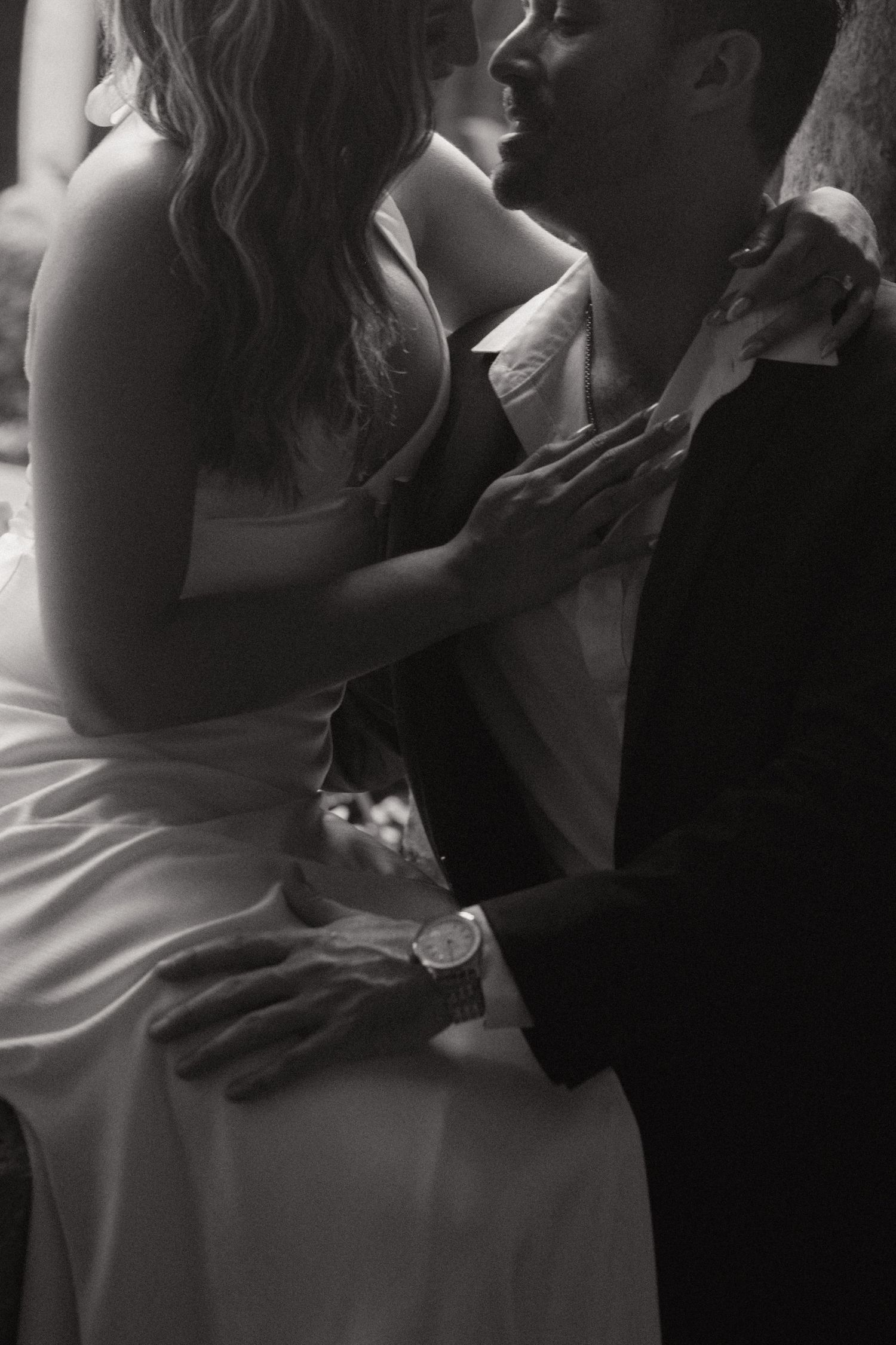 Black and white photo of a couple in an intimate embrace, a woman in a silk dress seated close to a man in a dark suit jacket.
