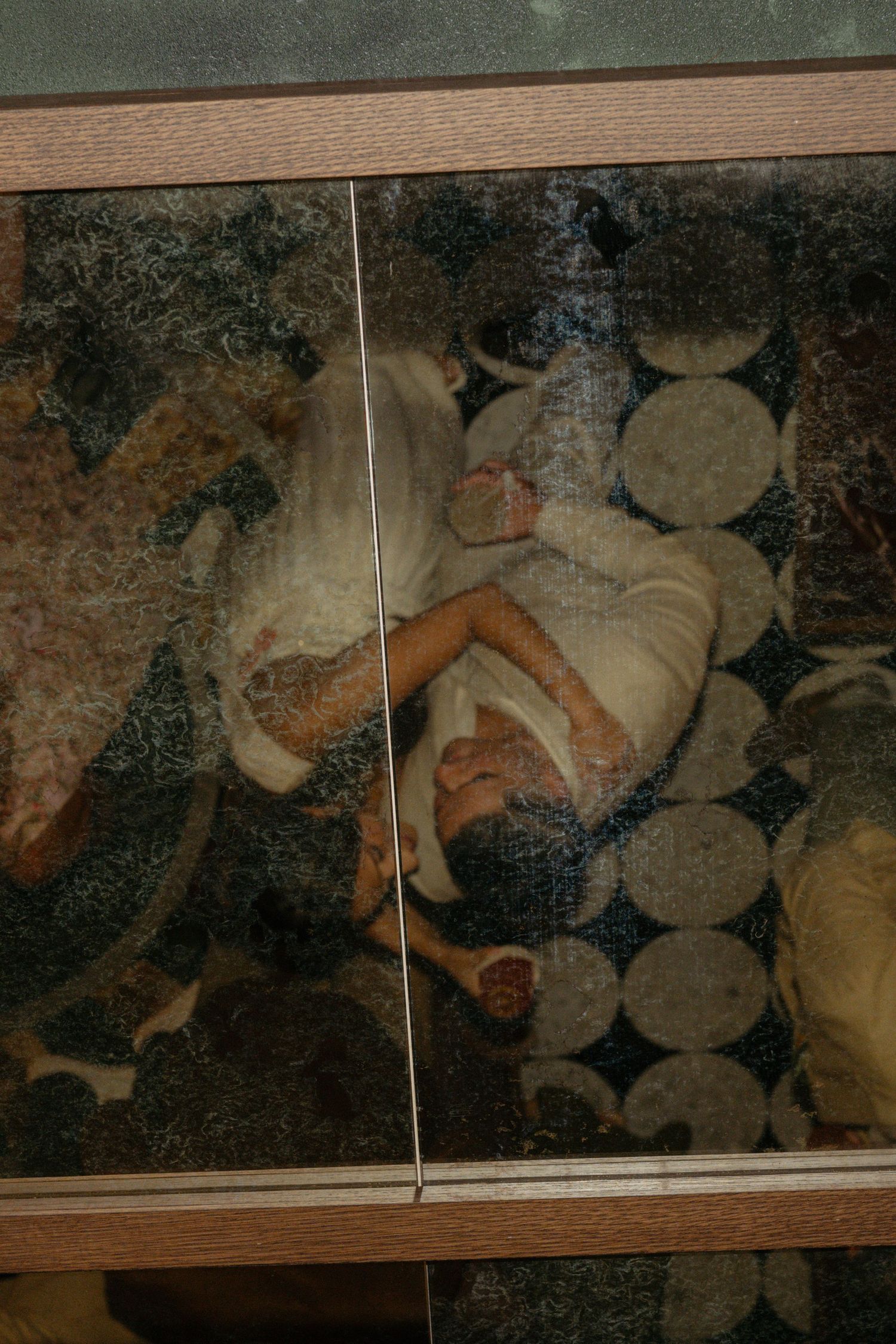 A reflected image of a person lying down, captured through a mirrored glass surface with a wooden frame.