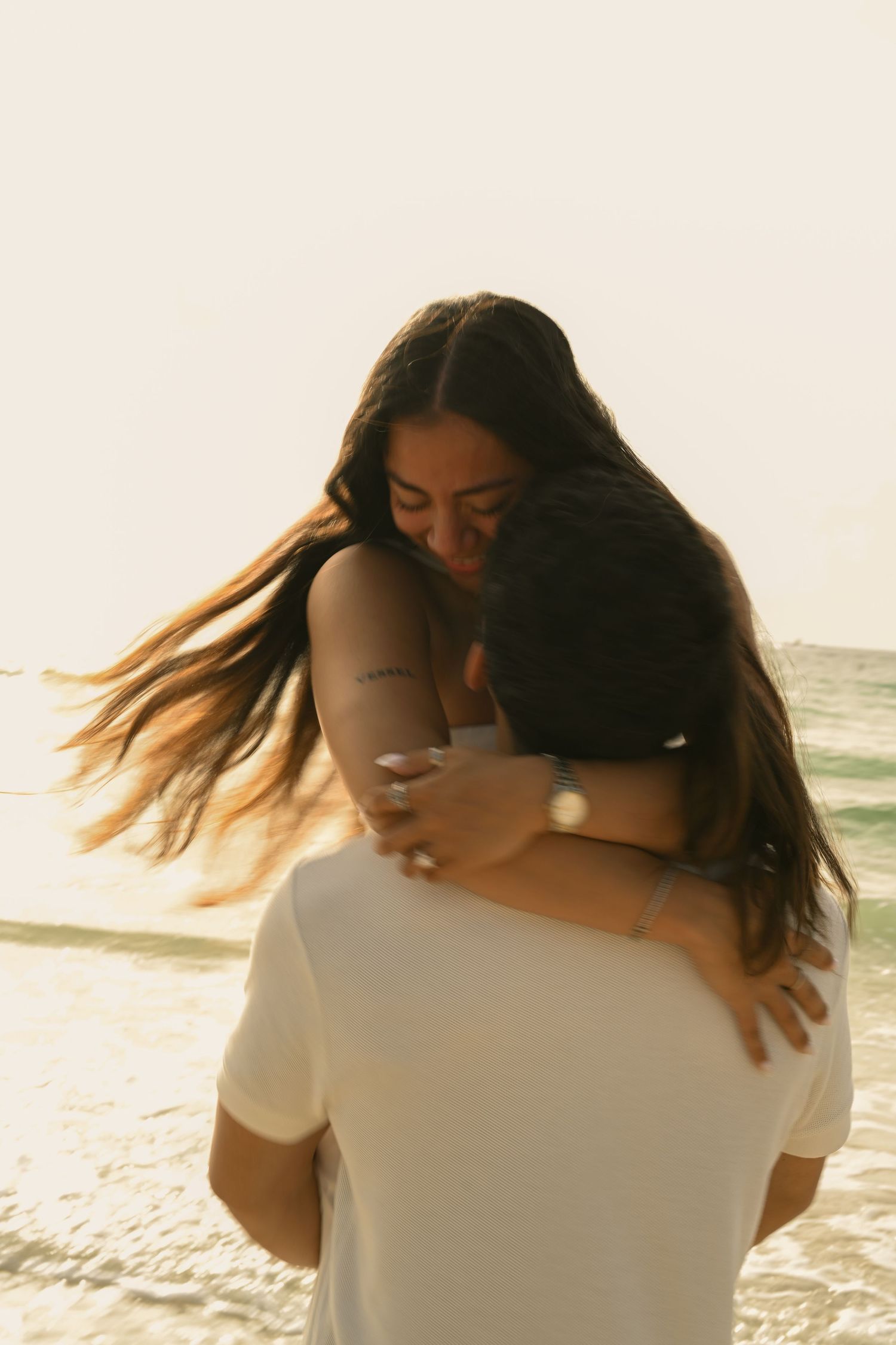A couple shares a romantic embrace with hair flowing in the ocean breeze.