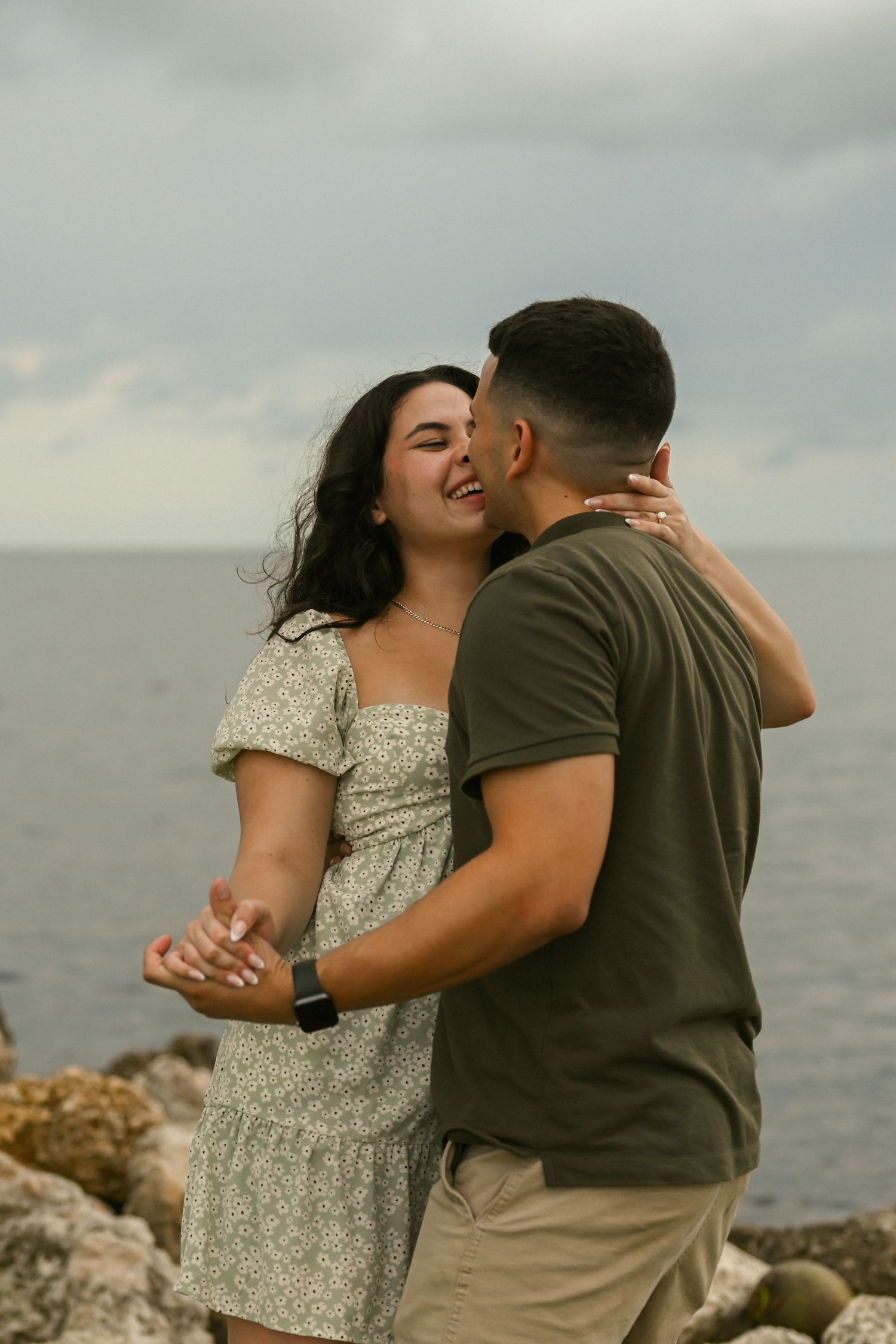A couple laughs together during a romantic moment by the ocean.