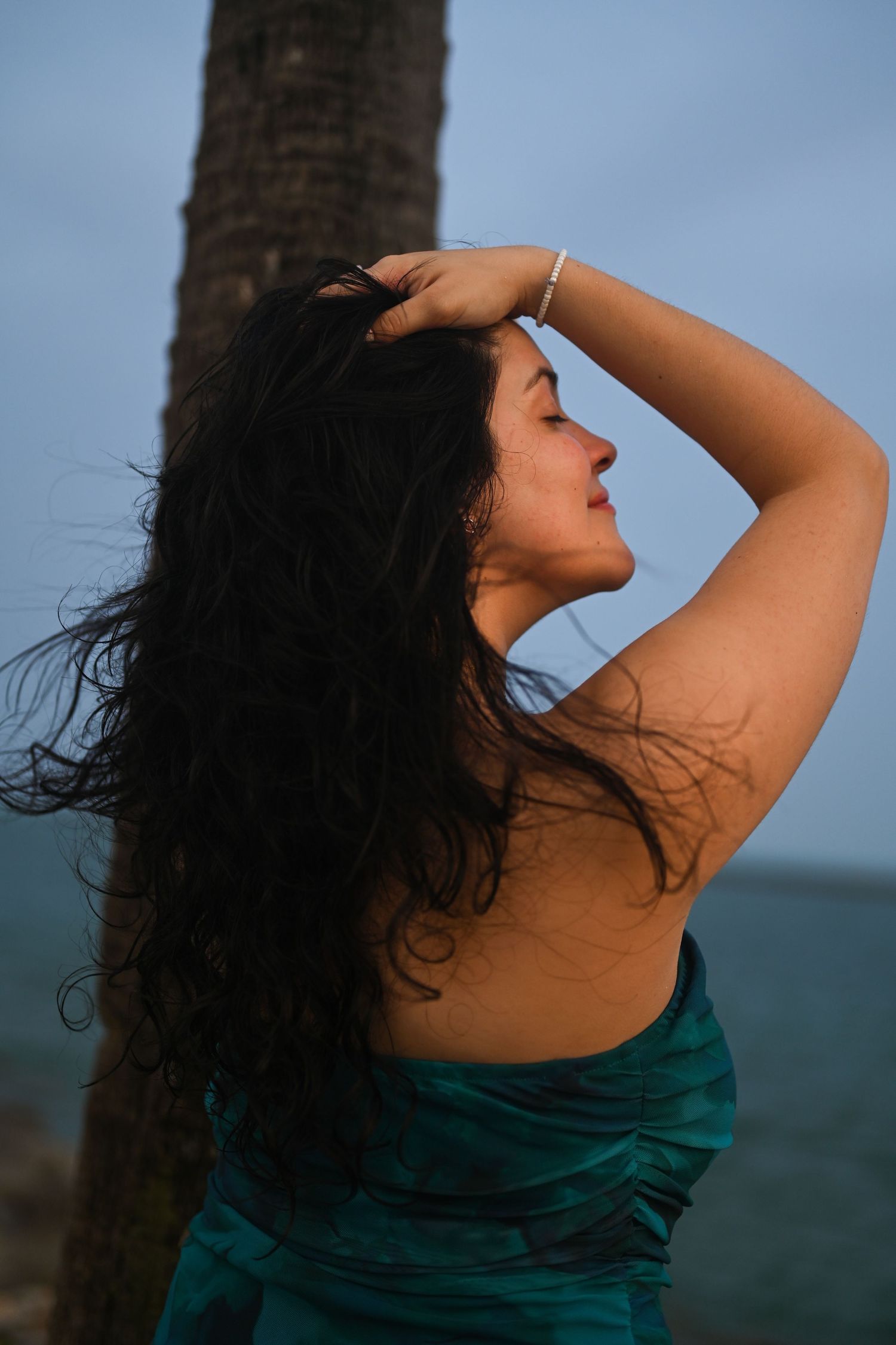 Artistic poses by palm tree with ocean view in teal dress.