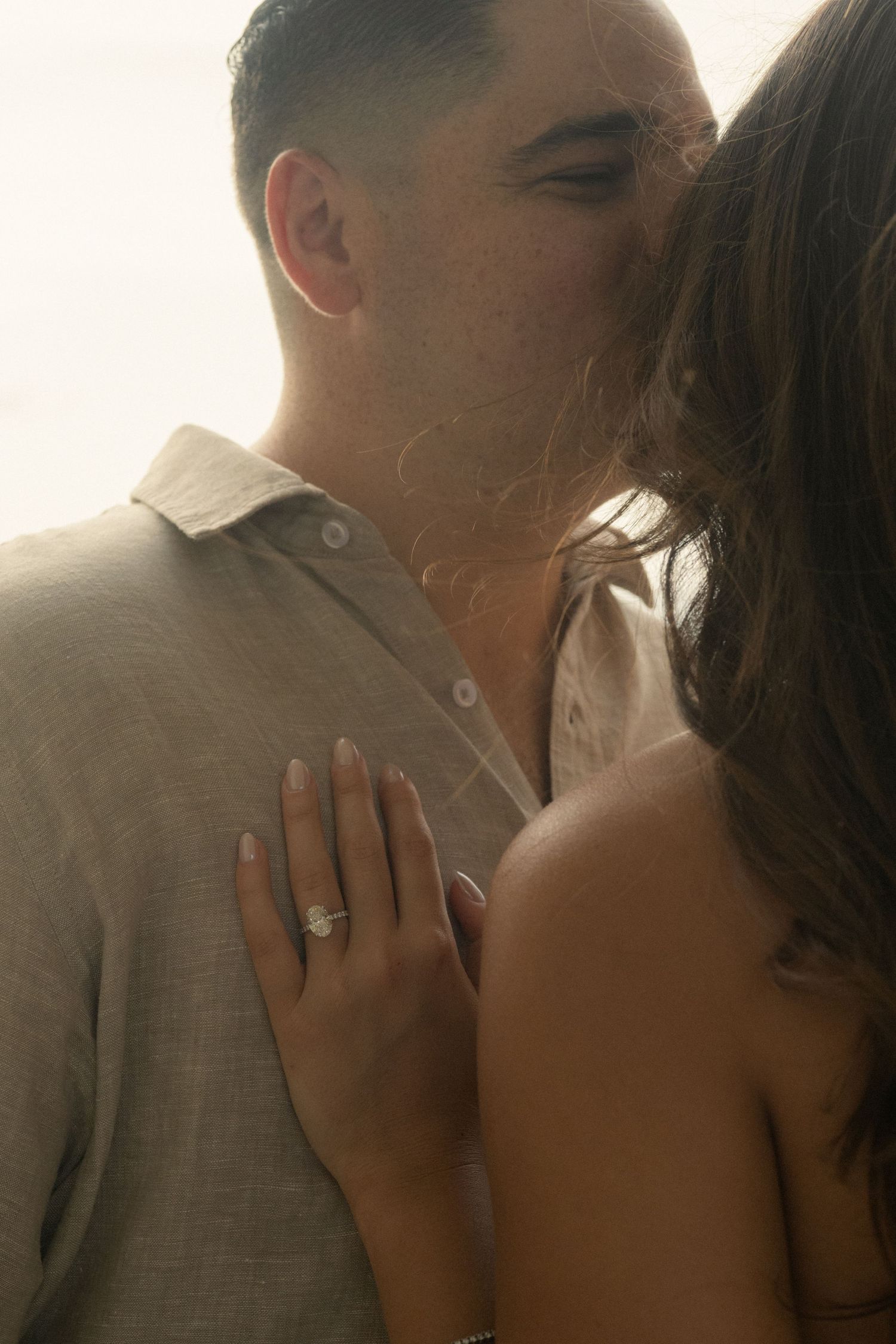 Couple sharing a tender moment, woman displaying an engagement ring on her hand against man's chest.