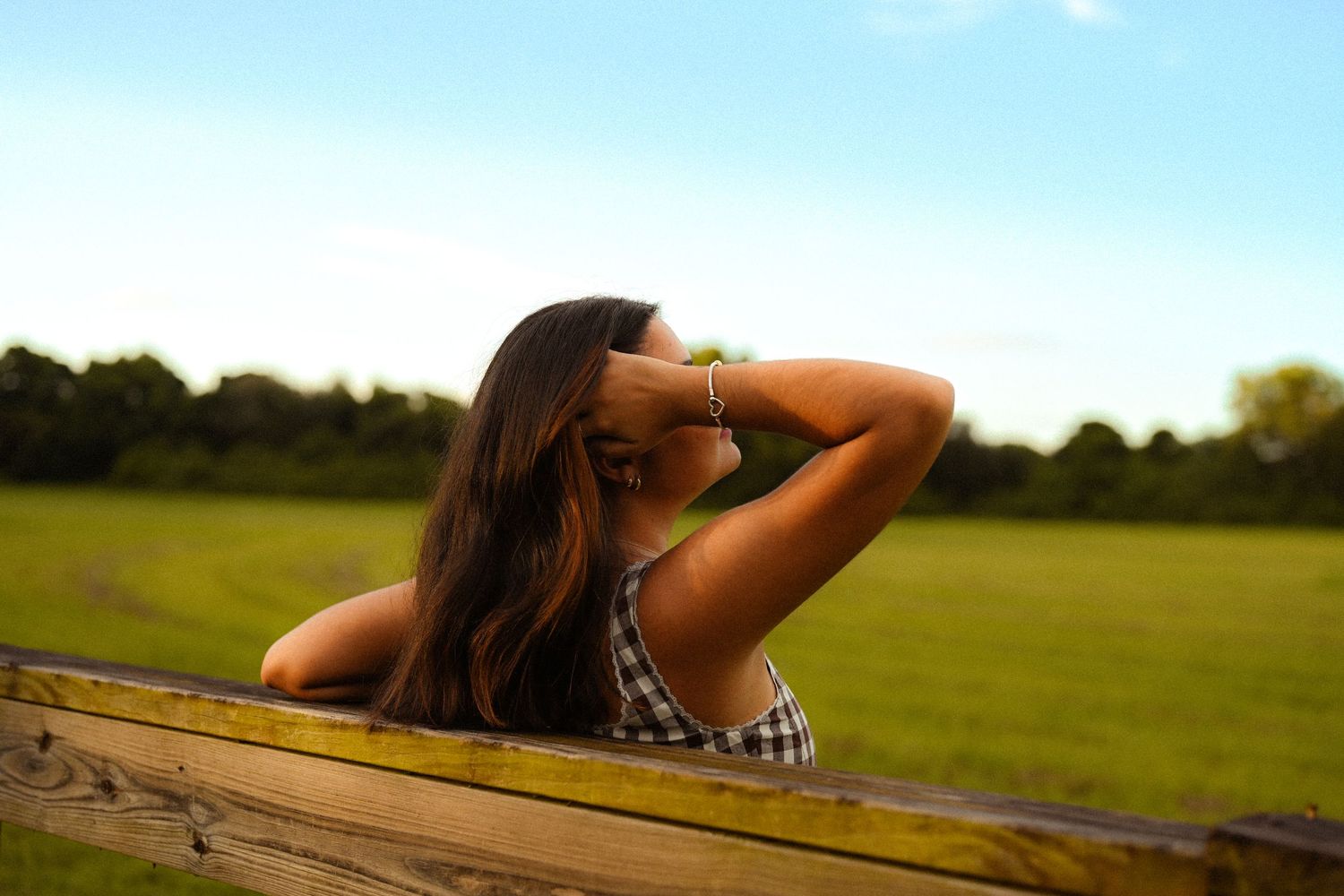 A gingham dress catches the sunlight while lounging on a wooden fence in a pastoral setting.