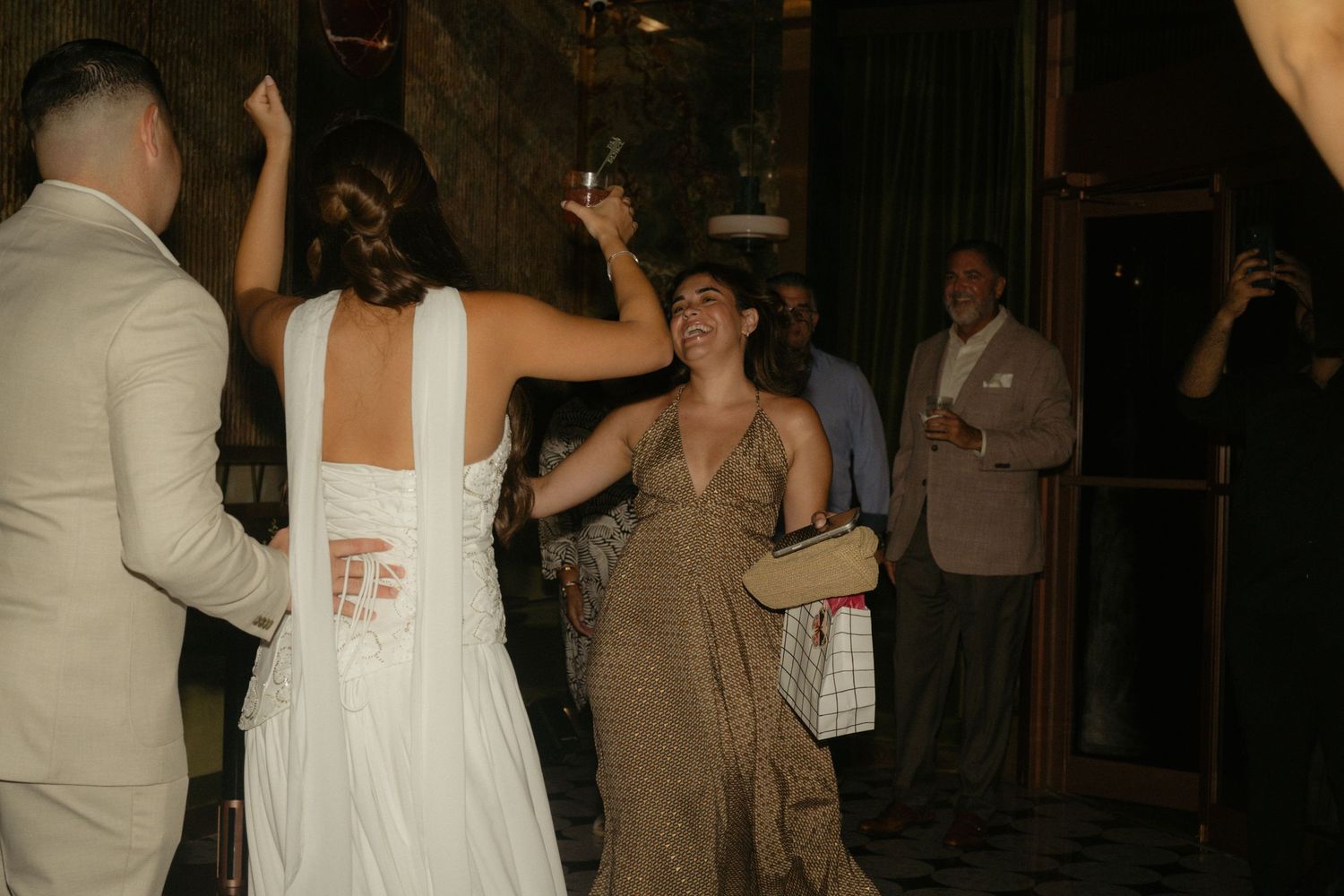 Bride in white backless gown dancing with guest in leopard dress at elegant wedding reception.
