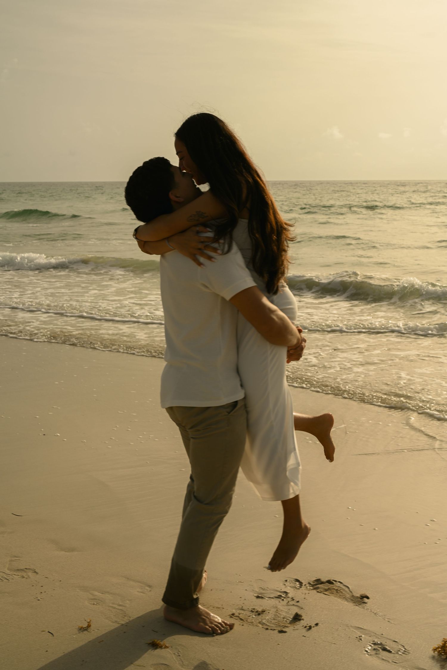 A couple shares a joyful embrace on the beach at sunset.