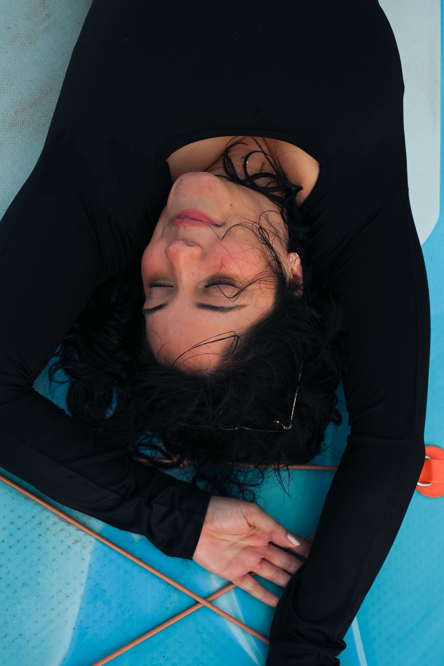 Person lying on blue surfboard showing relaxed expression against beach backdrop.