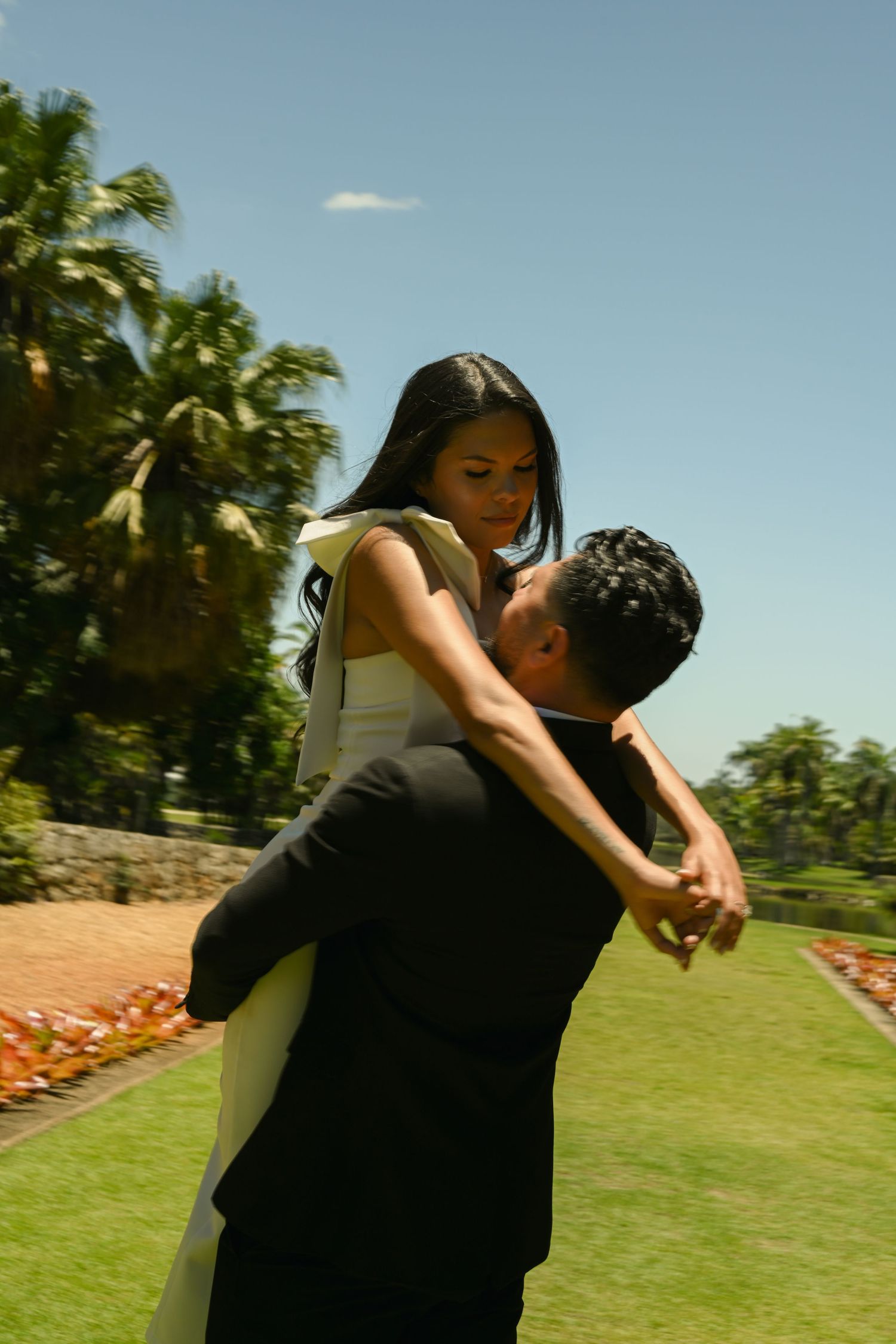 A couple shares an intimate dance moment on a grassy lawn with palm trees in the background.