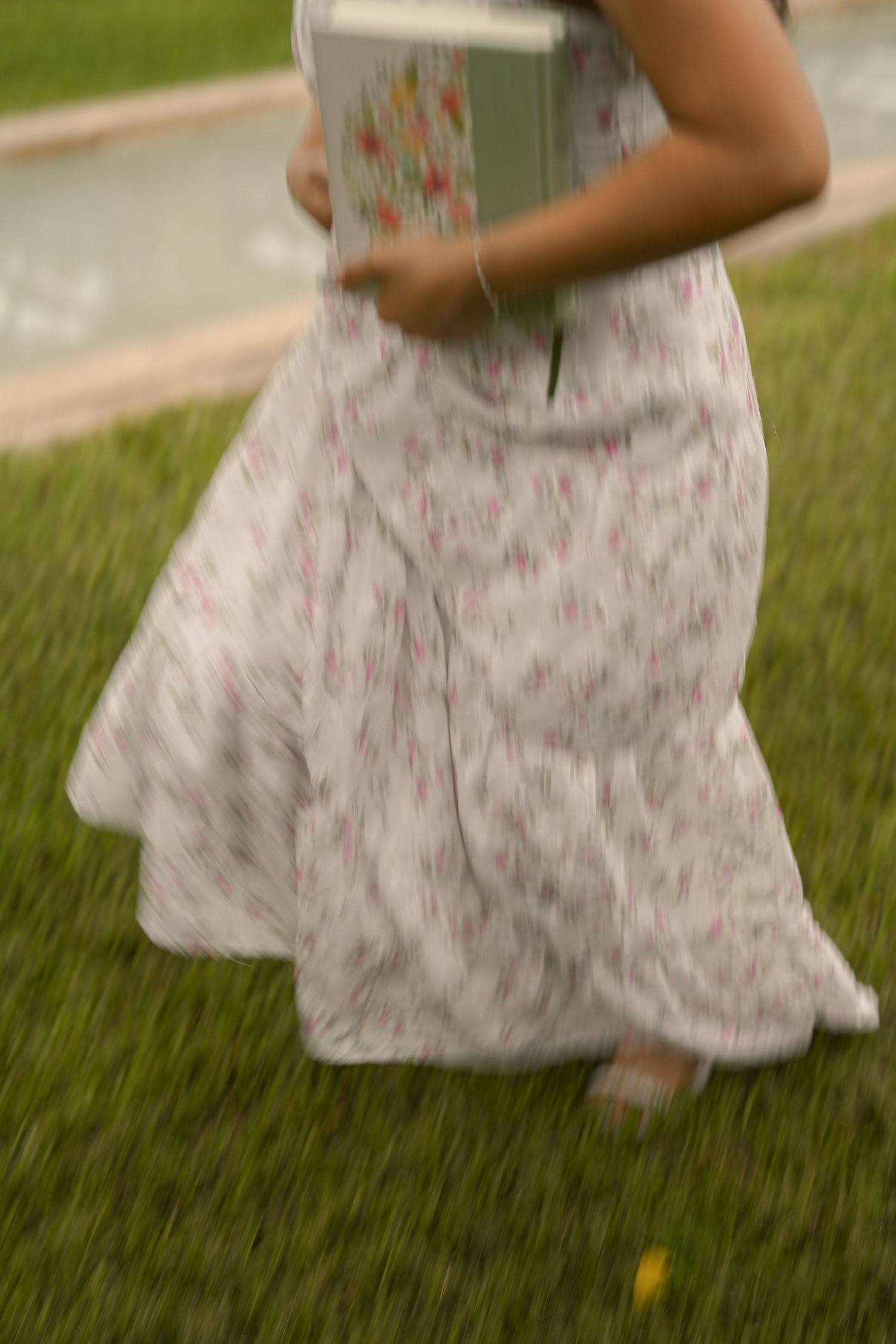 The hem of a flowing floral dress twirls against green grass in an artistic motion shot.