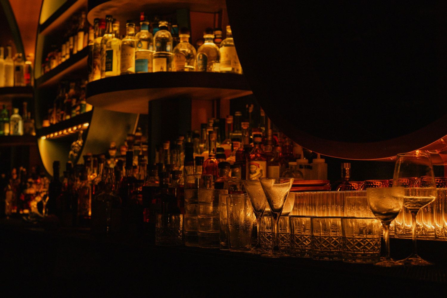 Dimly lit upscale bar with shelves of liquor bottles and martini glasses.