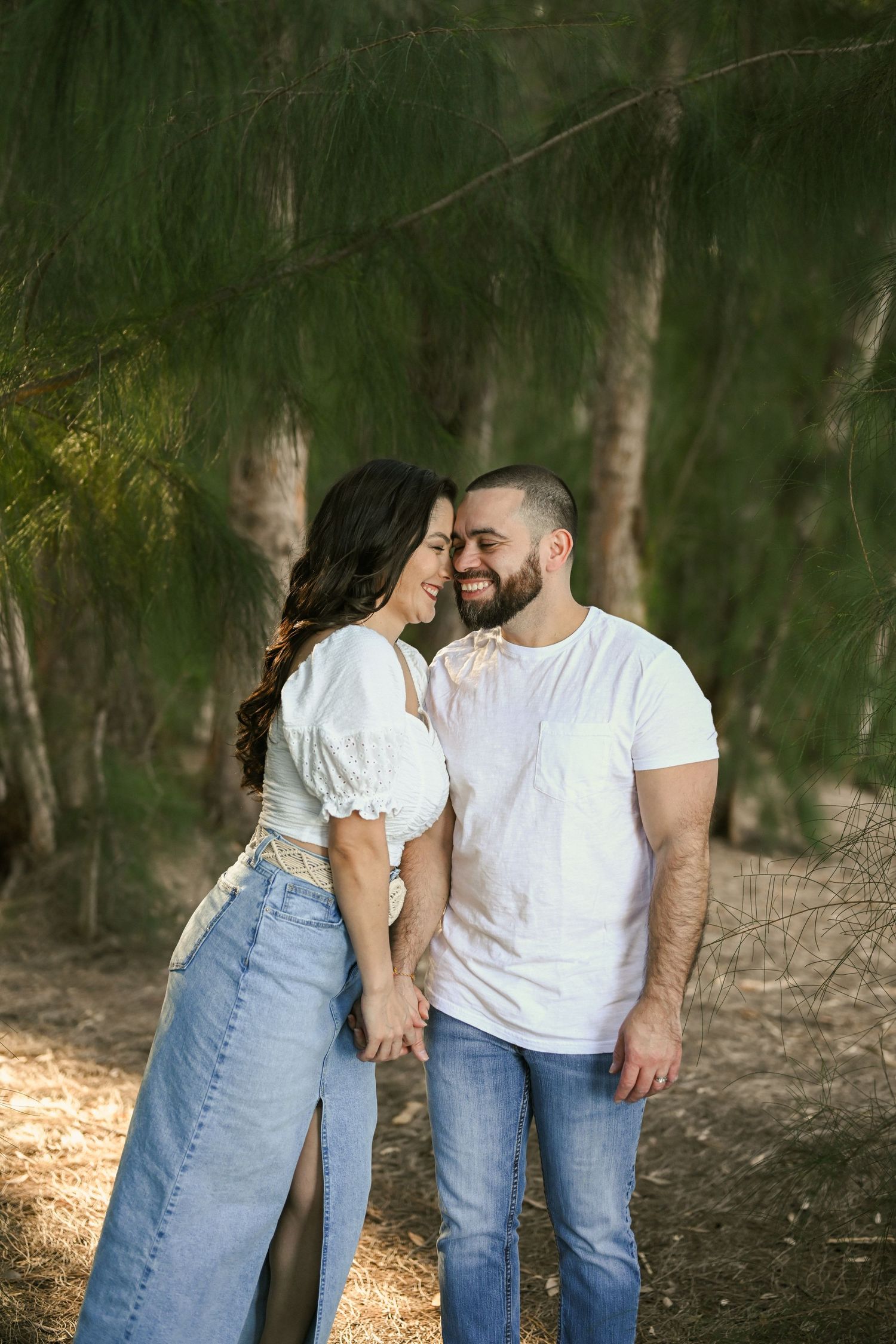 A couple in white shirts and jeans share an intimate moment in a wooded setting.