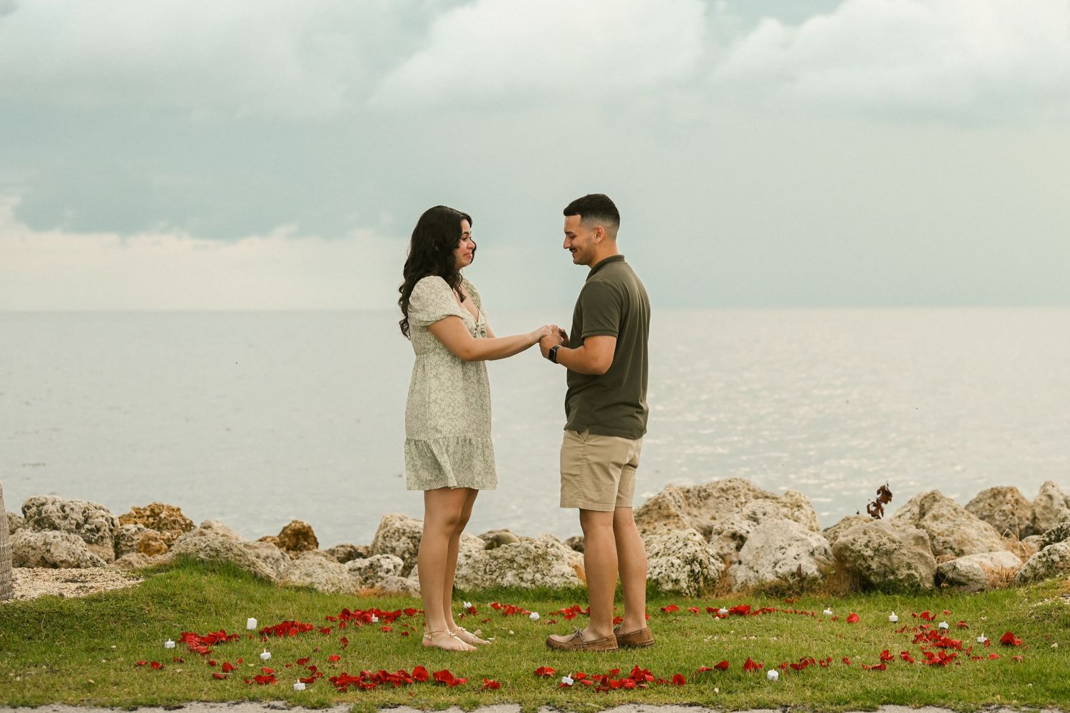 Two people share an emotional moment on a scenic coastal overlook with red flowers.
