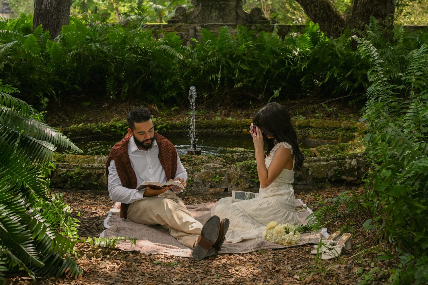 People relaxing and reading books in a peaceful garden setting surrounded by lush greenery and stone paths.