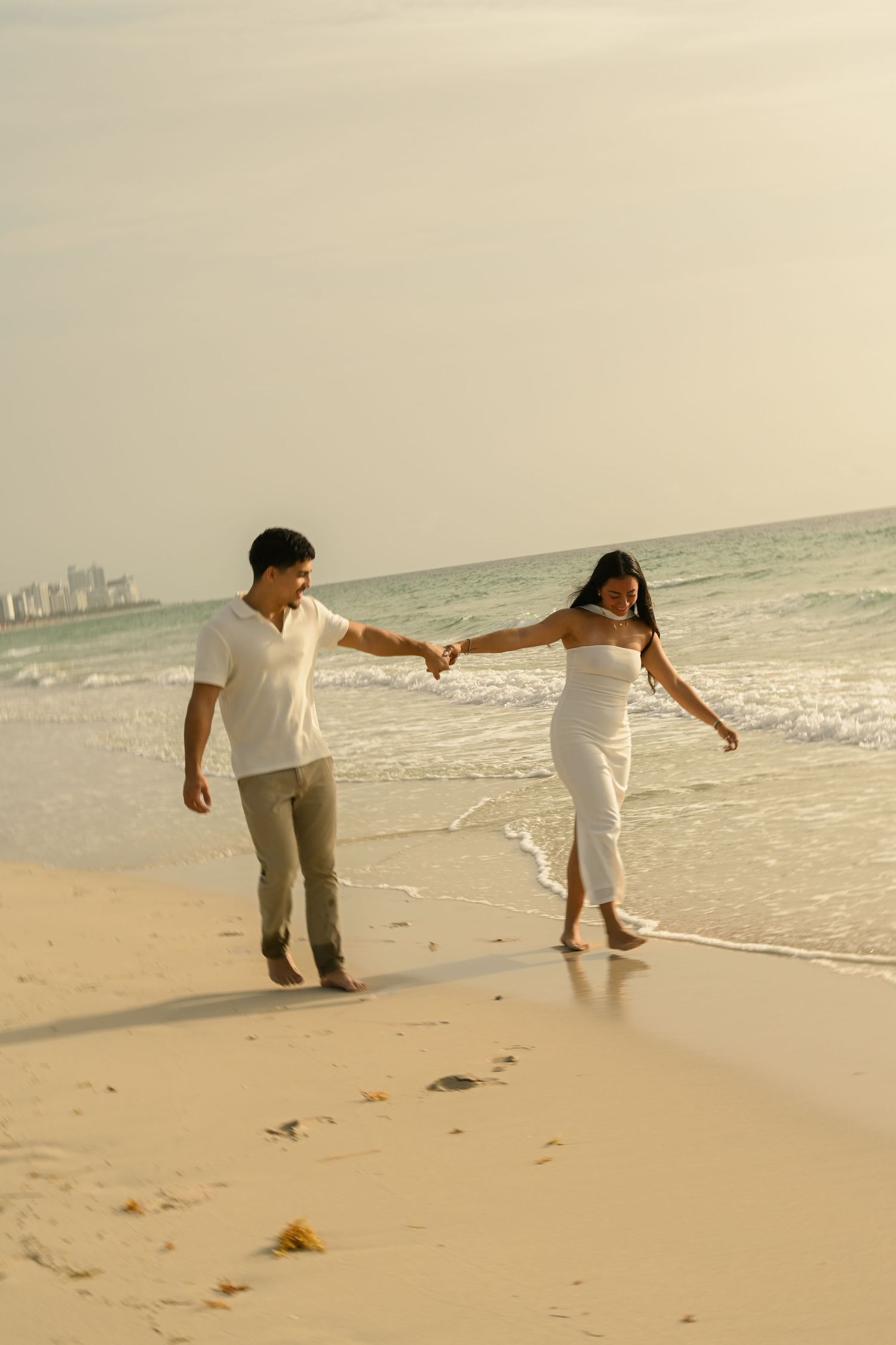 Romantic couple in white outfits dancing playfully on a sandy beach at sunset.