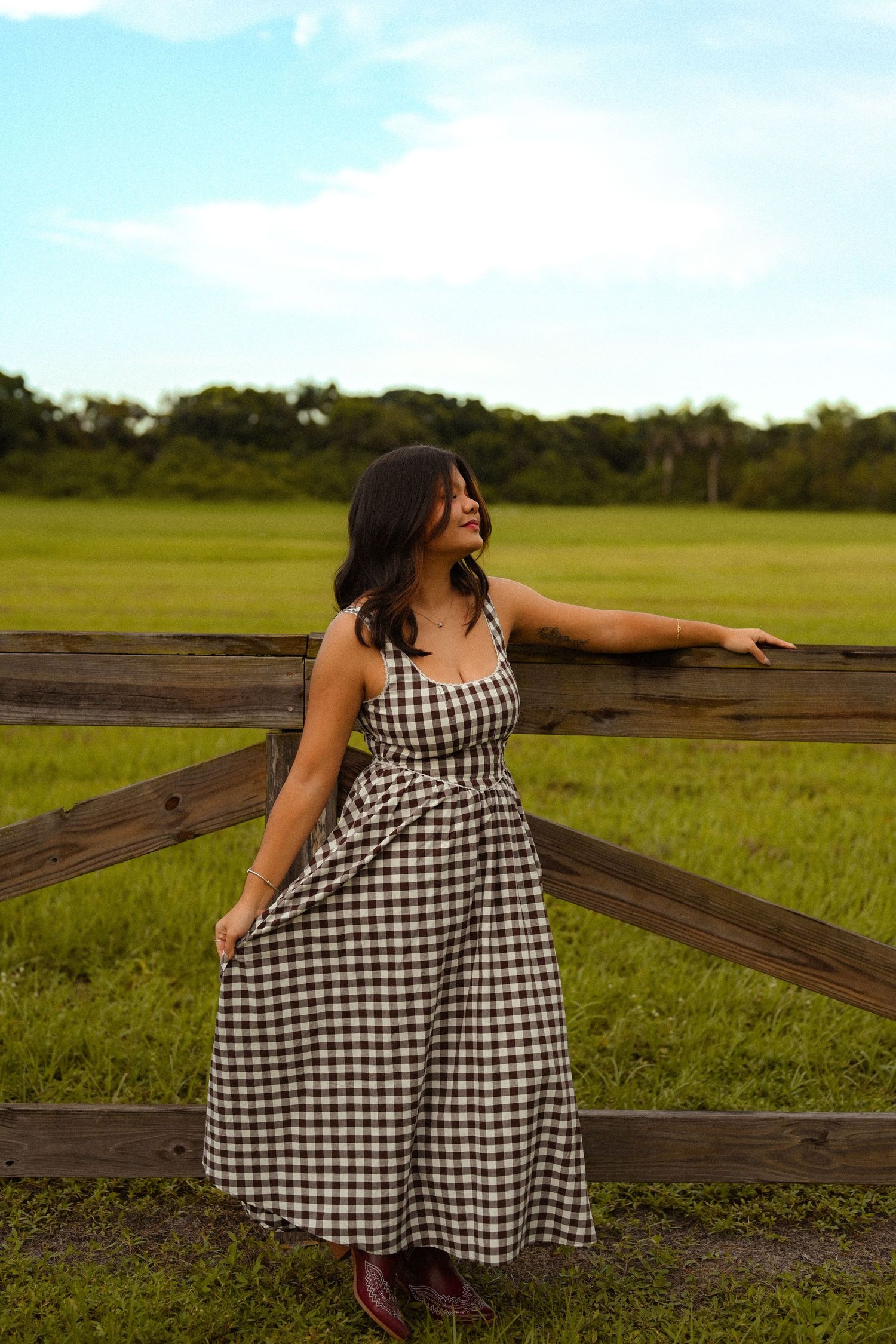 A black and white checkered dress stands out against a rustic wooden fence and green pasture.