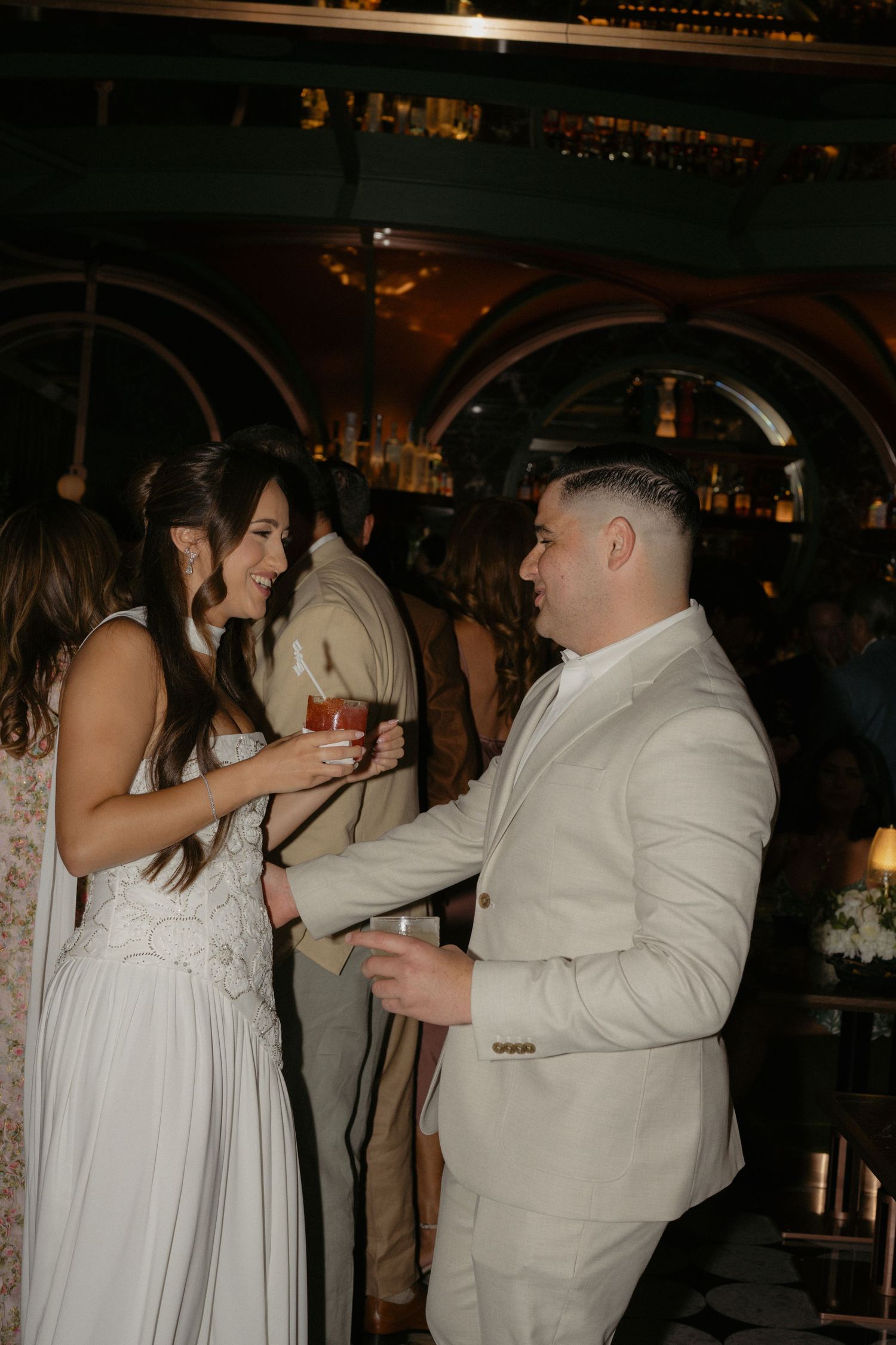 Bride and groom sharing a joyful moment at a bar during their wedding reception, holding cocktails.