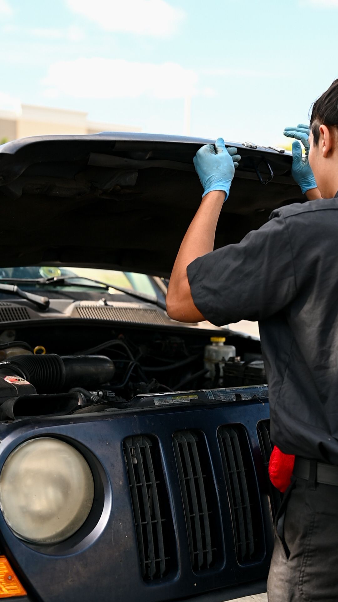 Automotive technician inspecting under the hood of a black vehicle.
