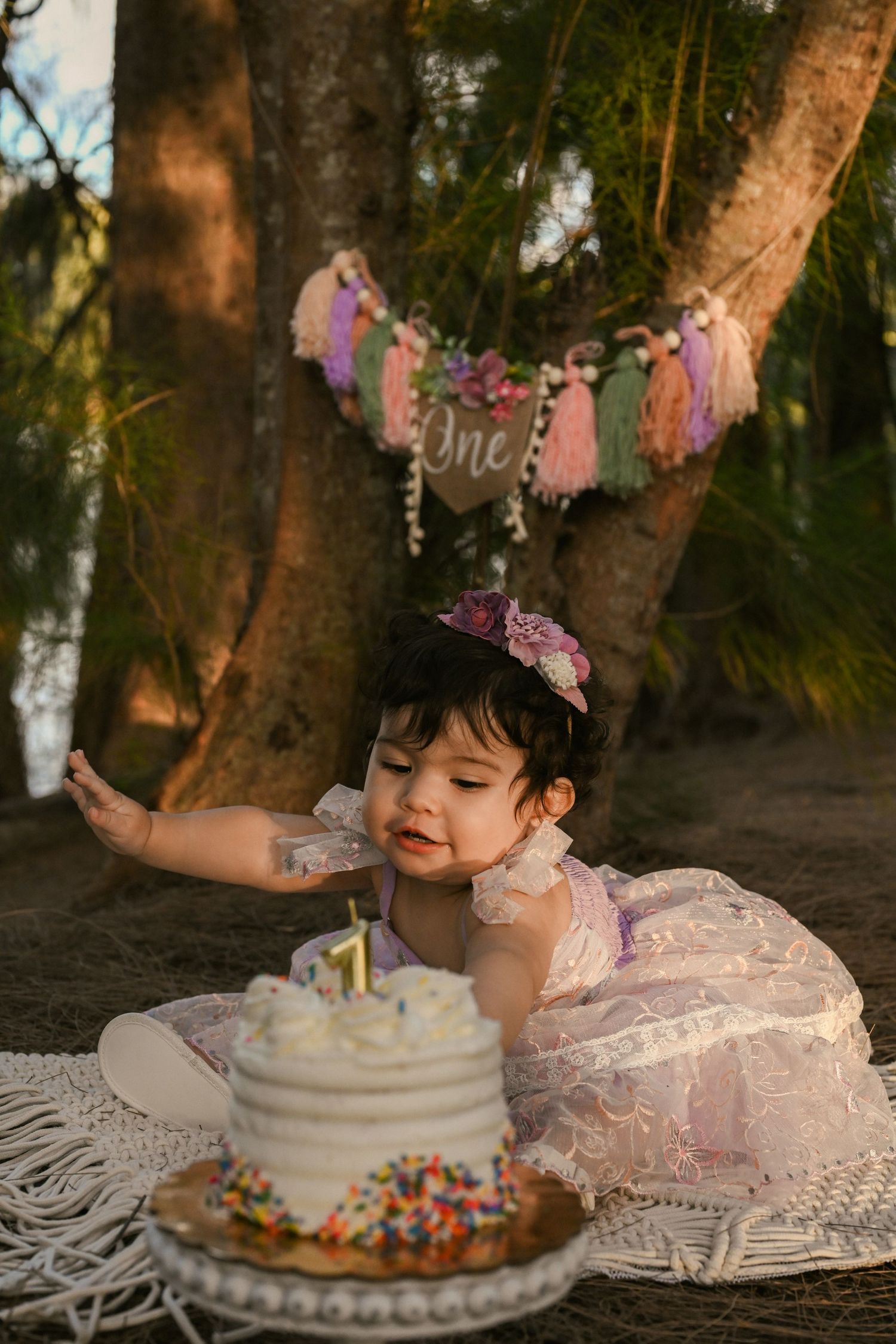 First birthday cake smash photo session with decorative banners and white frosted cake in outdoor setting.