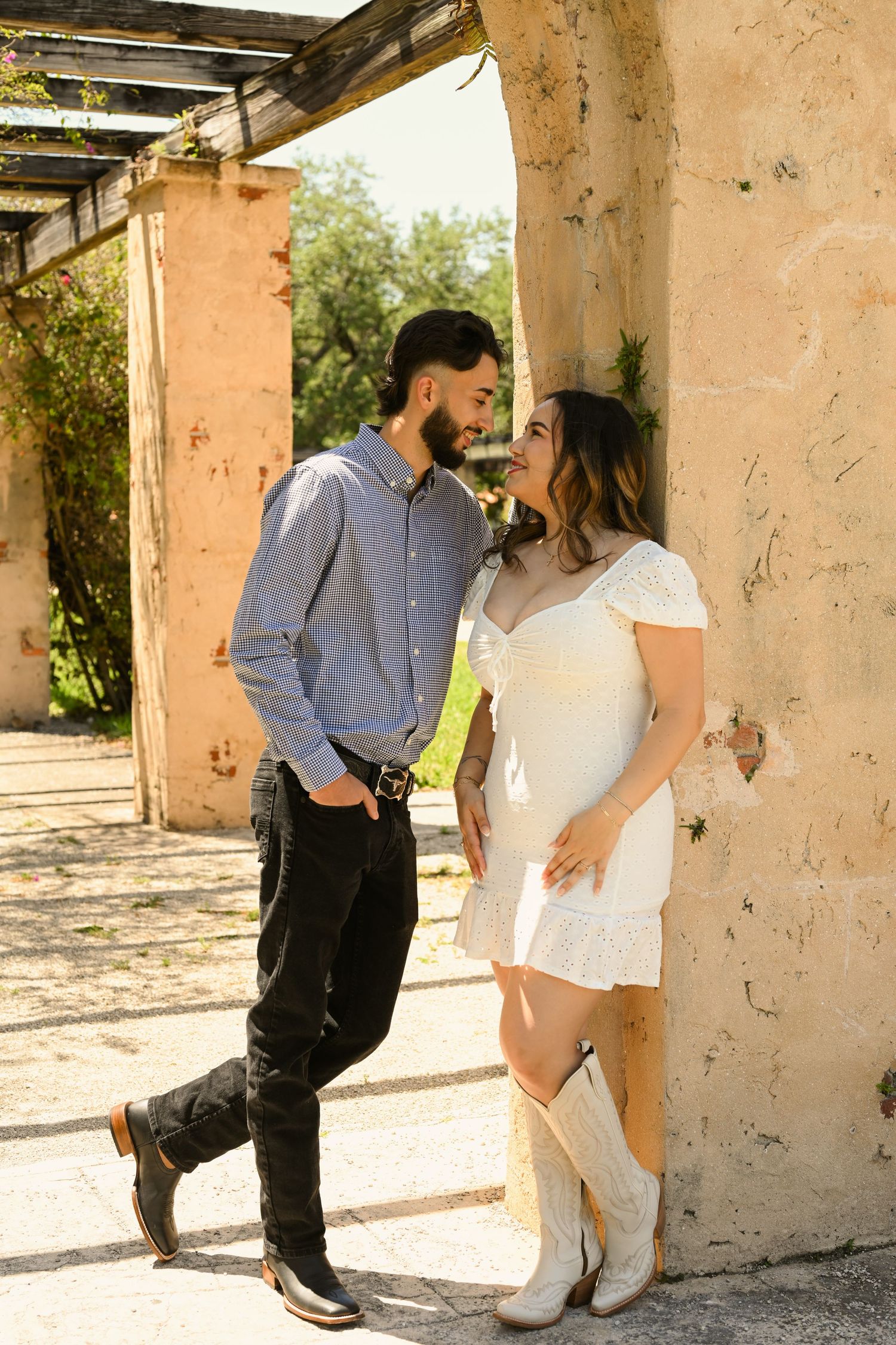 A couple poses playfully against a rustic wall in an engagement photoshoot.